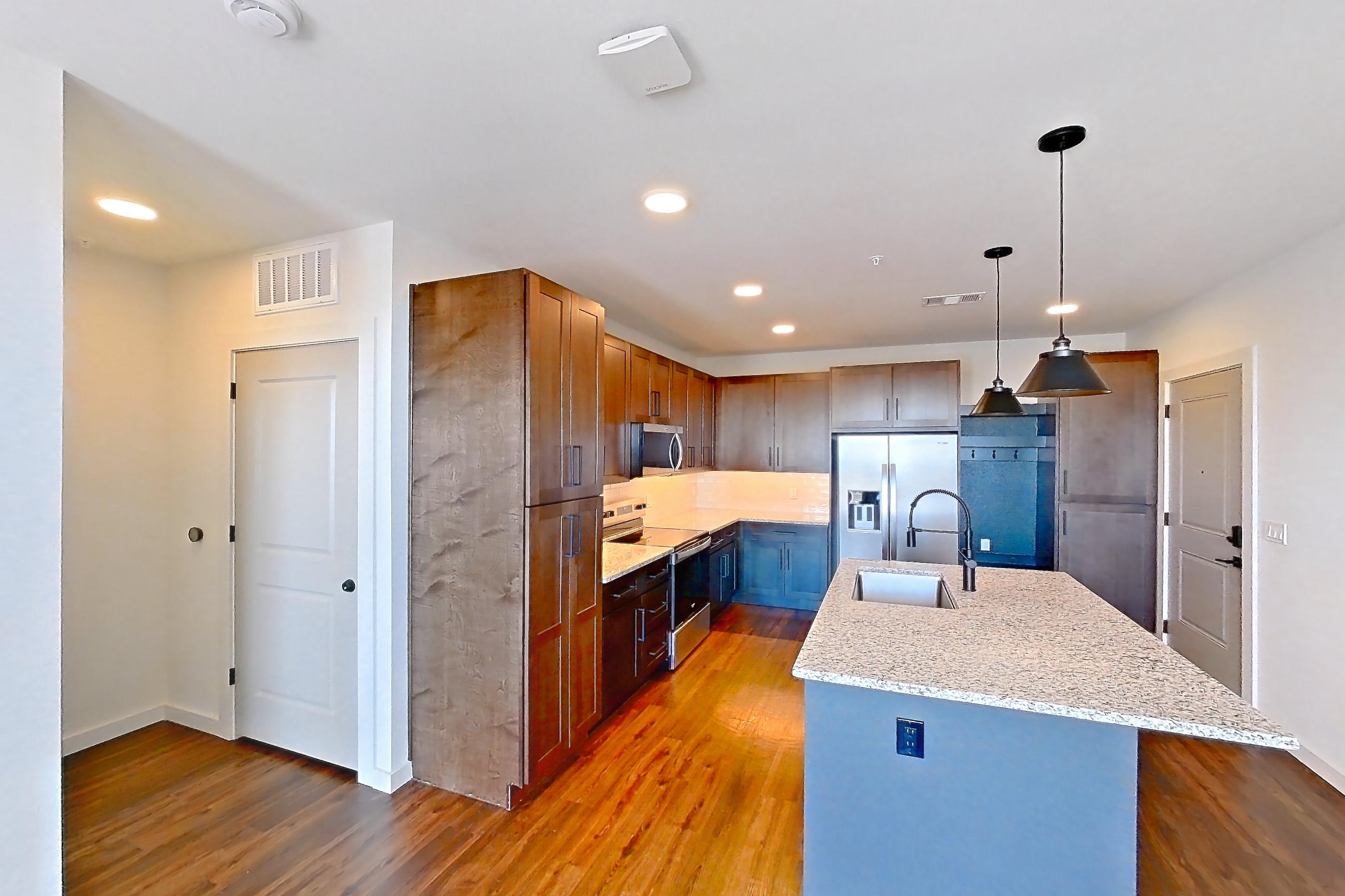 Living space with dark wood-finish flooring, electric range, kitchen island, light countertops, light stone countertops, oven/range, refrigerator, stainless steel appliances, and water & ice dispenser, Apartment 3-409 at Cortland Peterson