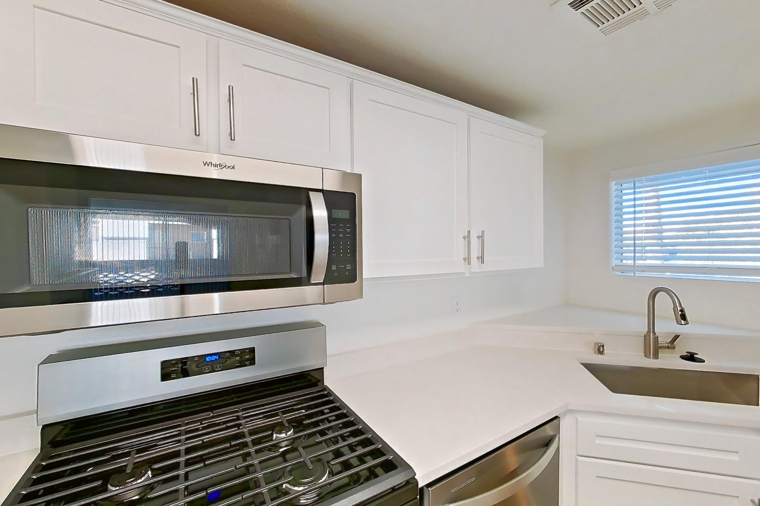 Kitchen with dishwasher, gas range, light countertops, light stone countertops, light wood-finish flooring, microwave, oven/range, refrigerator, and stainless steel appliances, Apartment 2001 at Monaco Park