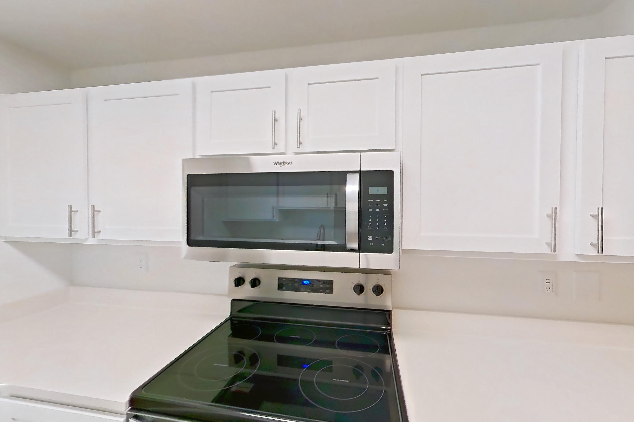 Kitchen with dishwasher, electric range, light countertops, light wood-finish flooring, microwave, oven/range, refrigerator, and stainless steel appliances, Apartment 01-2004 at Xander 3900