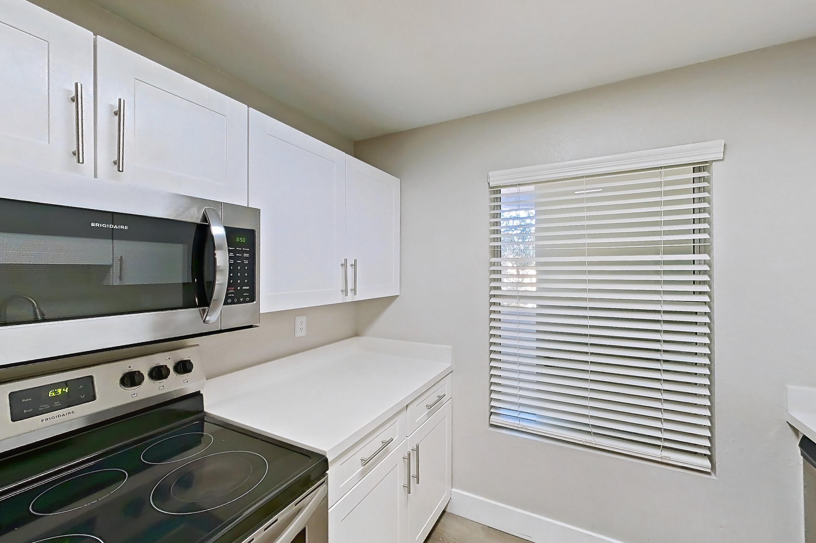 Kitchen with dishwasher, electric range, light countertops, light wood-finish flooring, microwave, oven/range, and stainless steel appliances, Apartment 14-2107 at Xander 3900