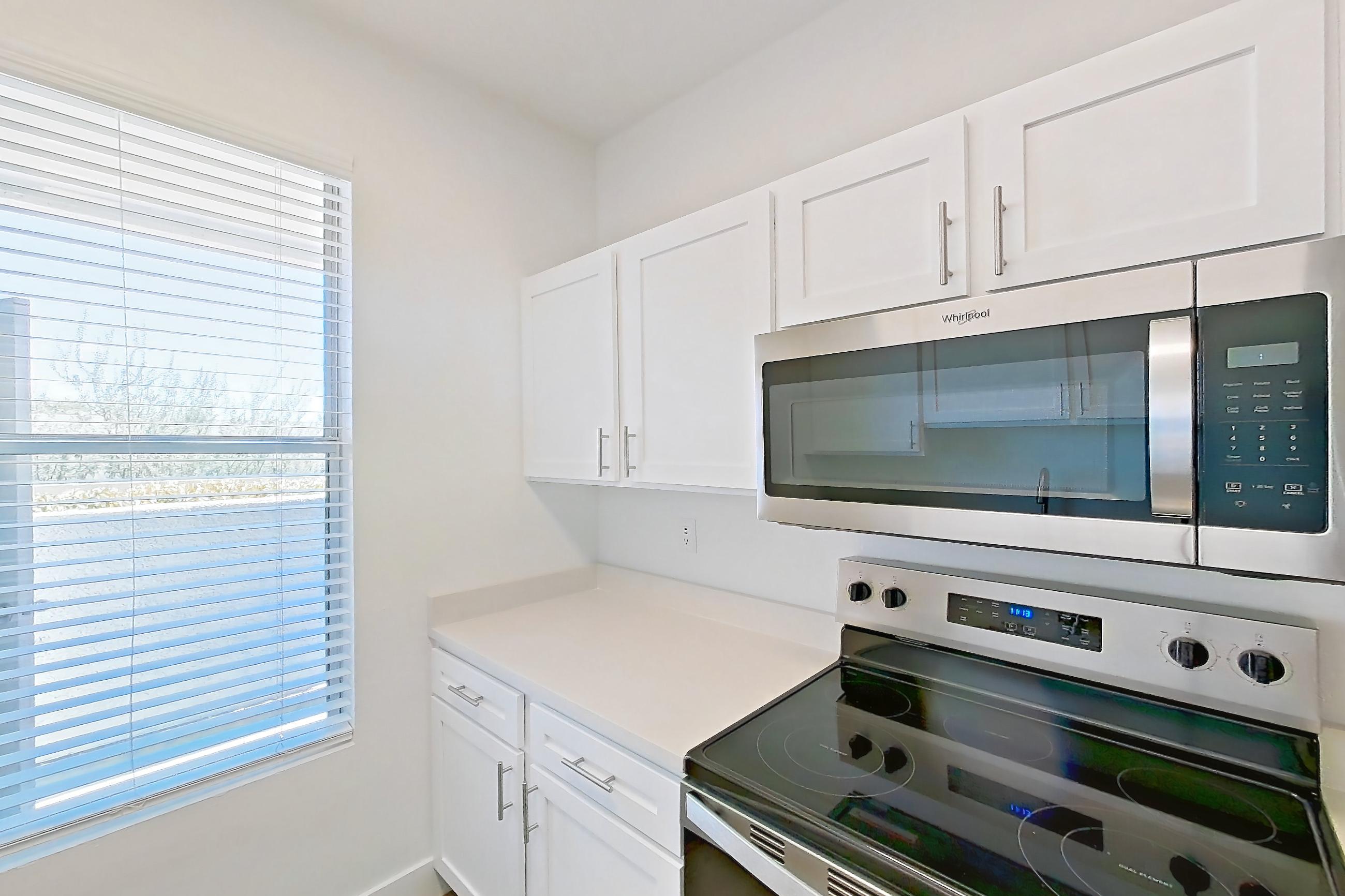 Kitchen with dishwasher, electric range, light countertops, light stone countertops, light wood-finish flooring, microwave, oven/range, and stainless steel appliances, Apartment 18-1050 at Xander 3900