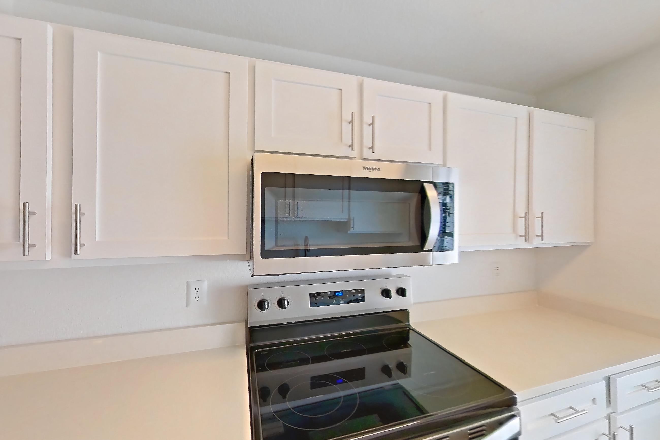Kitchen with dishwasher, electric range, light countertops, light stone countertops, light wood-finish flooring, microwave, oven/range, refrigerator, and stainless steel appliances, Apartment 34-2089 at Xander 3900