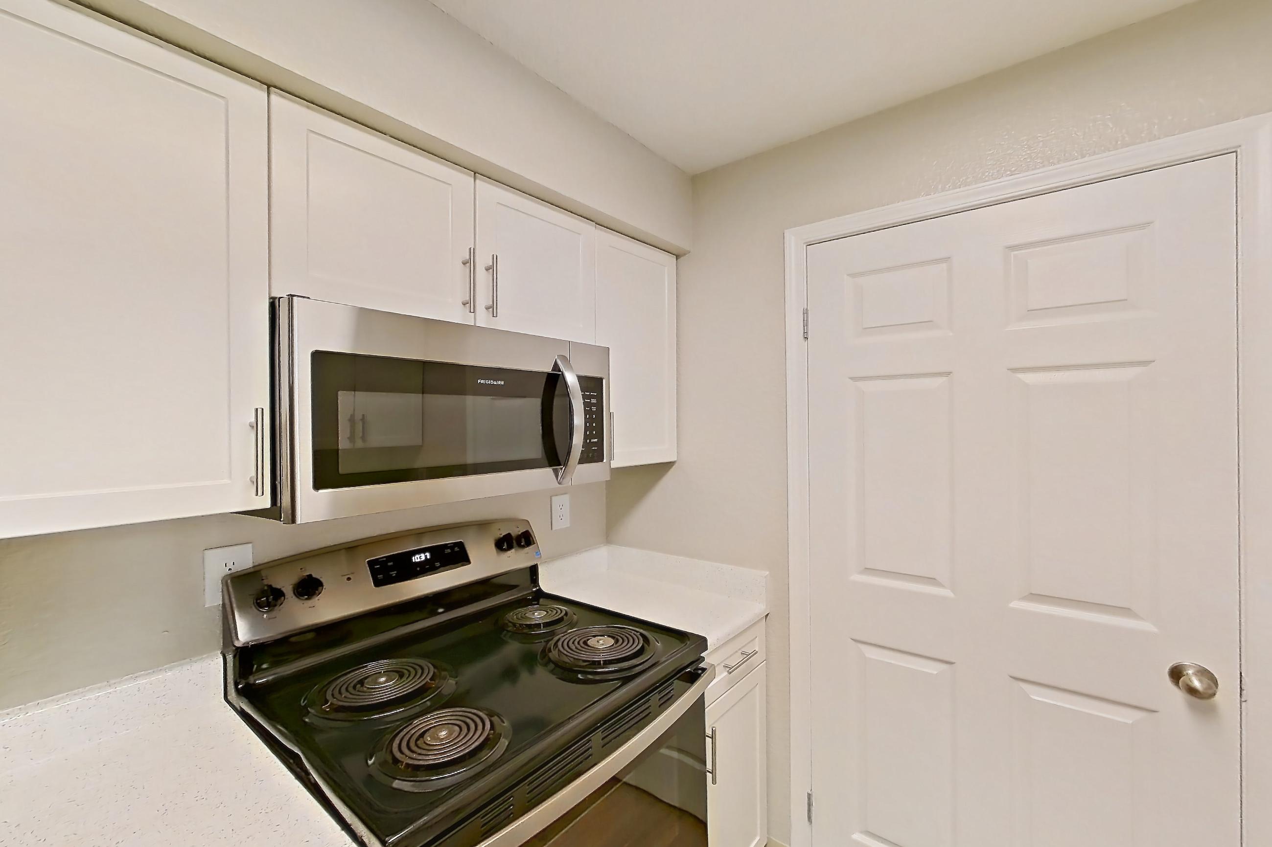 Kitchen with dishwasher, electric range, light countertops, light stone countertops, light wood-finish flooring, microwave, oven/range, refrigerator, and stainless steel appliances, Apartment 30-2084 at Xander 3900