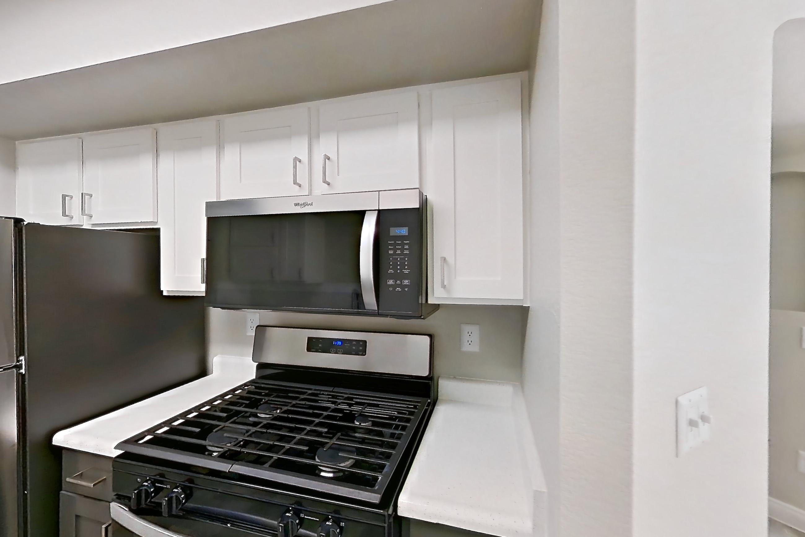 Kitchen with gas range, in-unit laundry, light countertops, light wood-finish flooring, microwave, oven/range, refrigerator, and stainless steel appliances, Apartment 1018 at Vintage Pointe