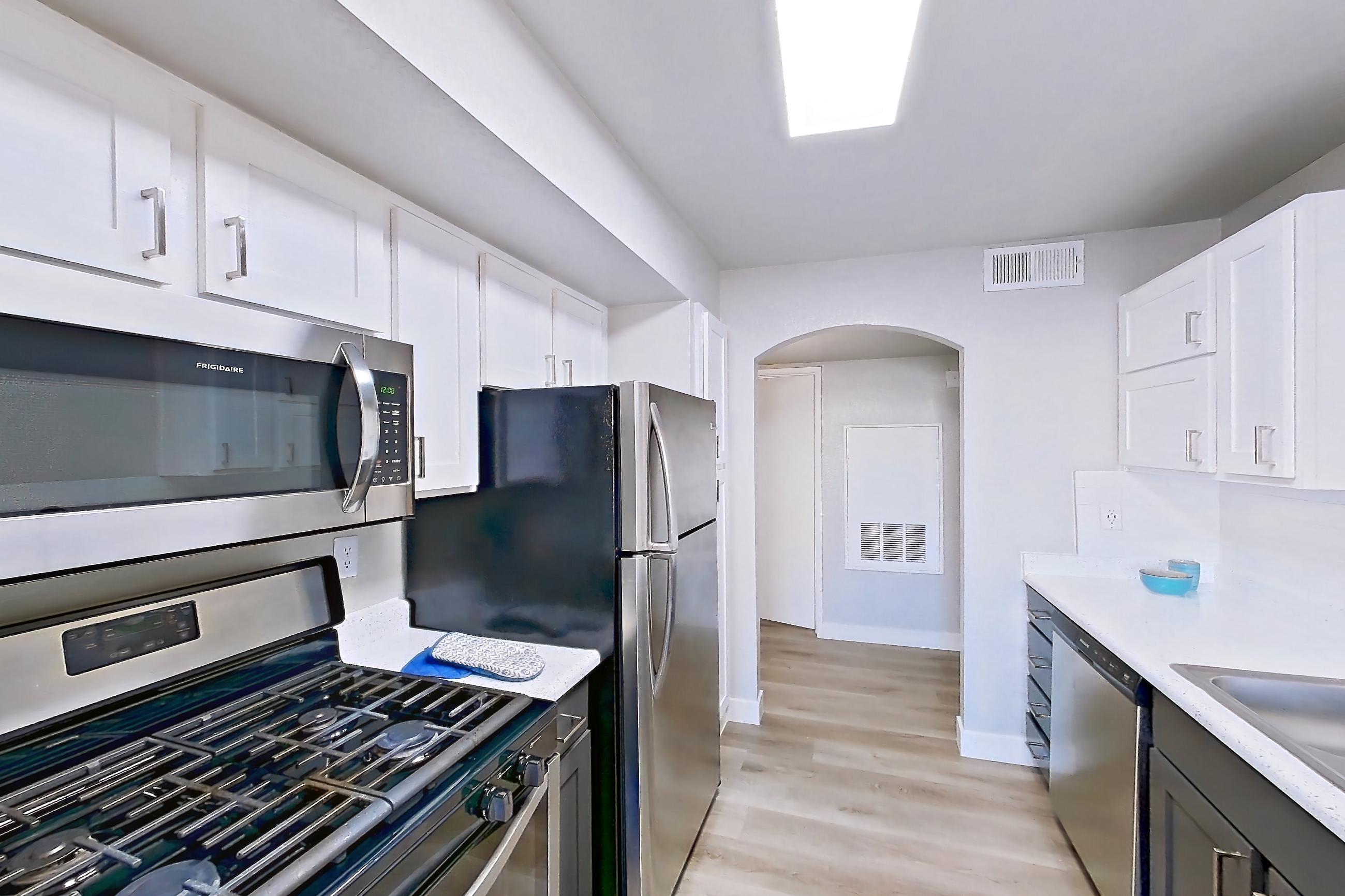Kitchen with dishwasher, gas range, light stone countertops, light wood-finish flooring, microwave, oven/range, refrigerator, and stainless steel appliances, Apartment 1109 at Vintage Pointe