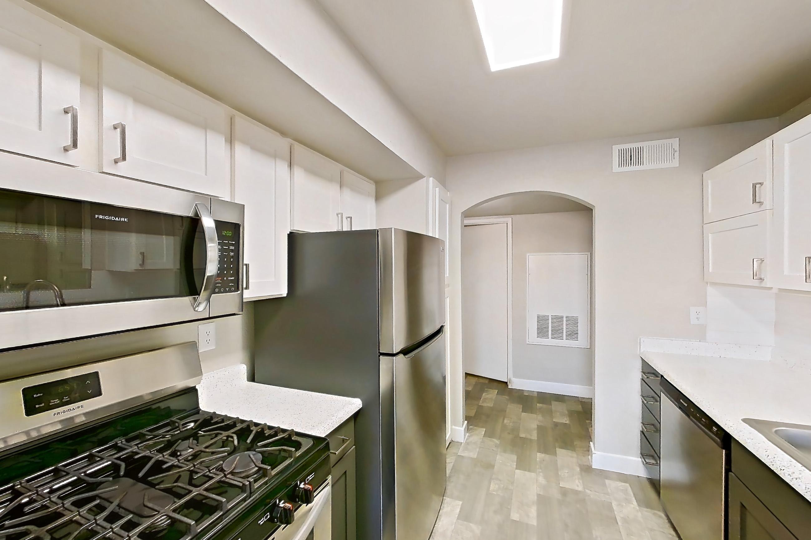 Kitchen with dishwasher, gas range, in-unit laundry, light stone countertops, light wood-finish flooring, microwave, oven/range, refrigerator, and stainless steel appliances, Apartment 1125 at Vintage Pointe
