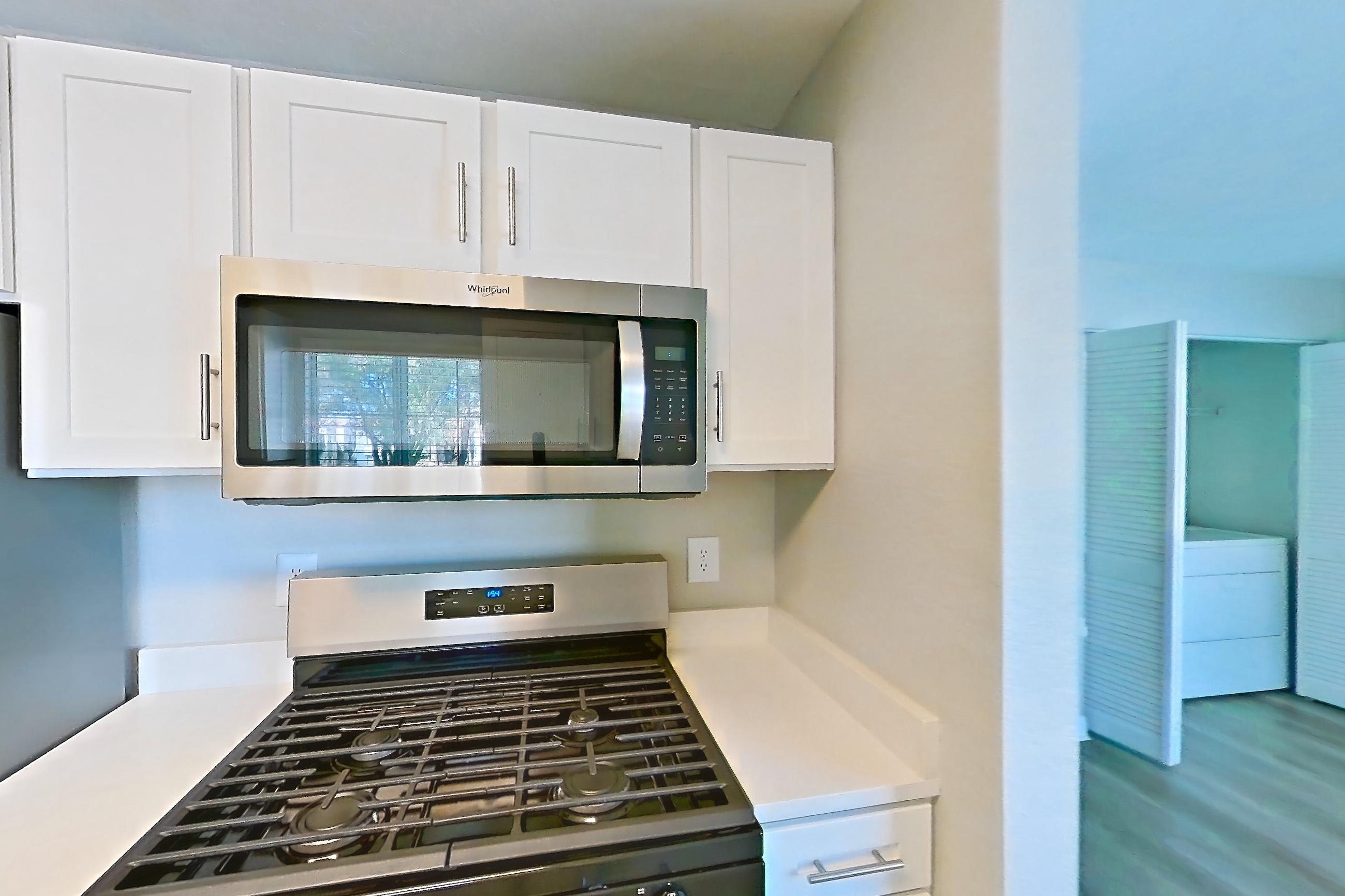 Kitchen with dishwasher, gas range, light countertops, light stone countertops, light wood-finish flooring, microwave, oven/range, refrigerator, and stainless steel appliances, Apartment 2020 at Vintage Pointe