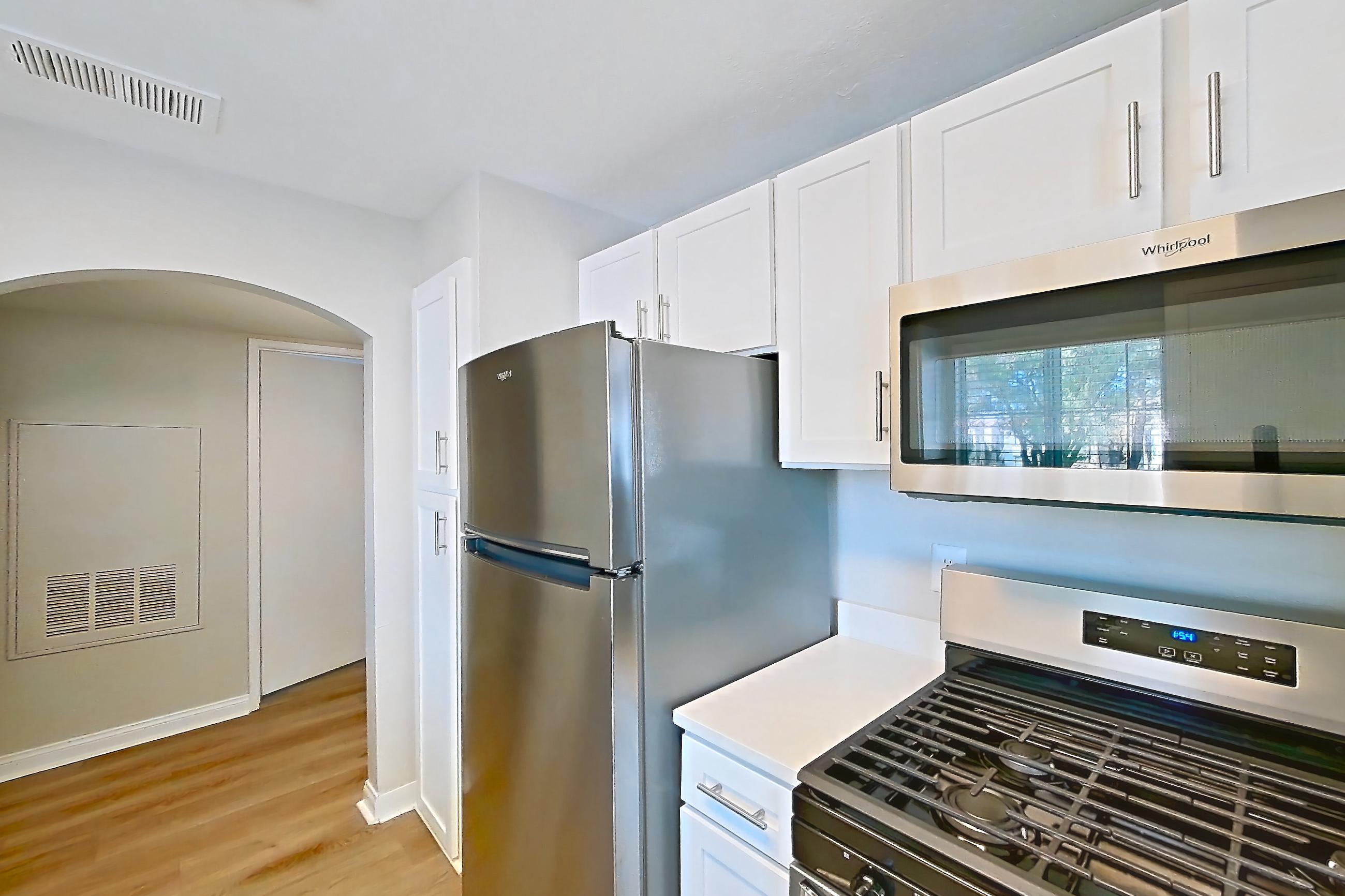 Kitchen with dishwasher, gas range, light countertops, light stone countertops, light wood-finish flooring, microwave, oven/range, refrigerator, and stainless steel appliances, Apartment 2020 at Vintage Pointe
