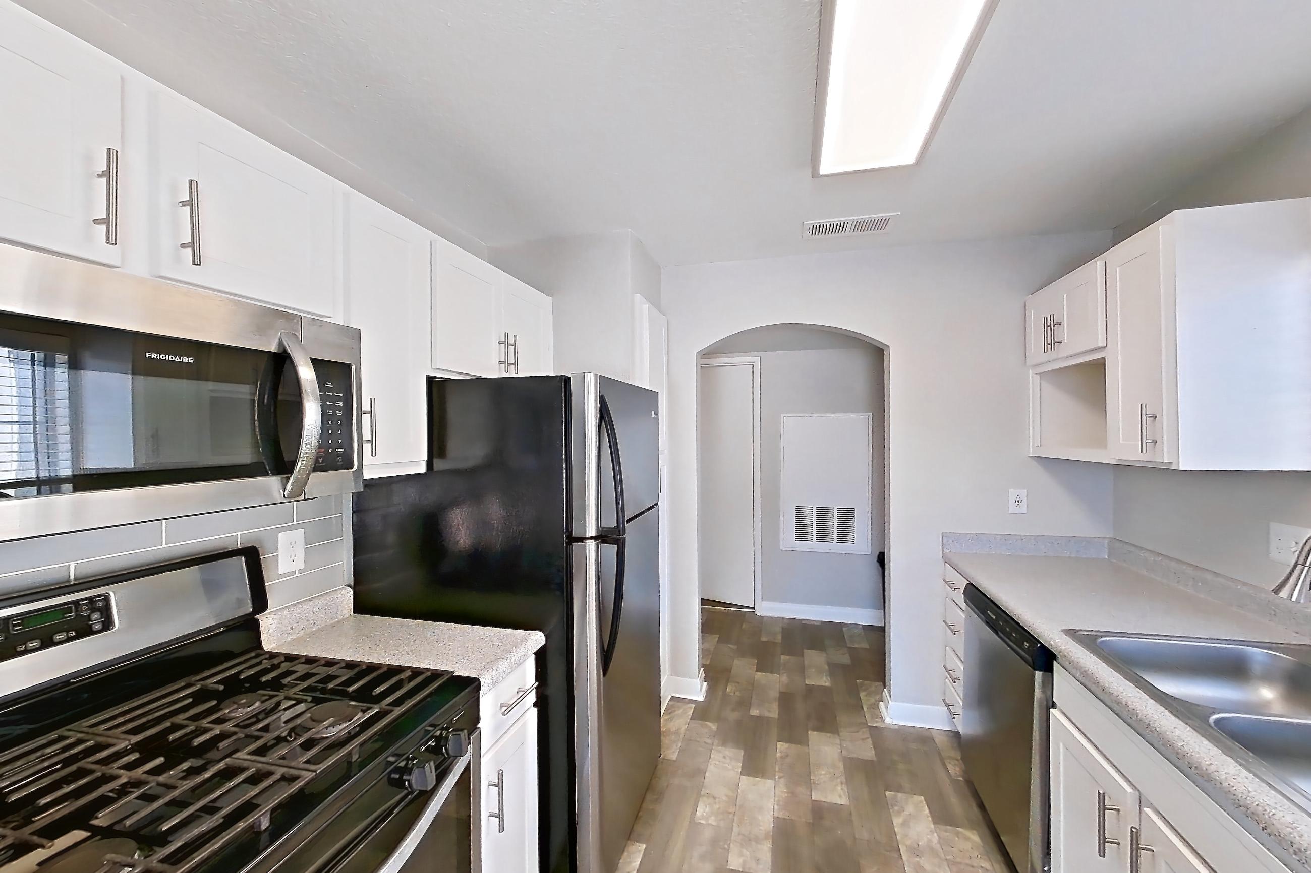 Kitchen with dishwasher, gas range, in-unit laundry, light countertops, light stone countertops, light wood-finish flooring, microwave, oven/range, refrigerator, and stainless steel appliances, Apartment 2081 at Vintage Pointe