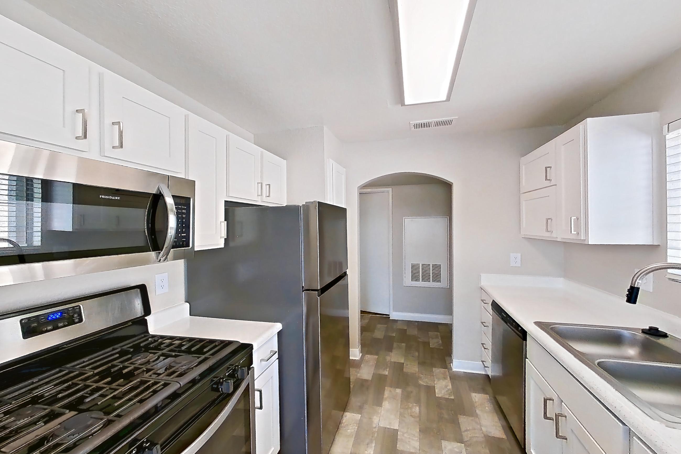 Kitchen with dishwasher, gas range, light countertops, light stone countertops, light wood-finish flooring, microwave, oven/range, refrigerator, stainless steel appliances, and white appliances, Apartment 2089 at Vintage Pointe