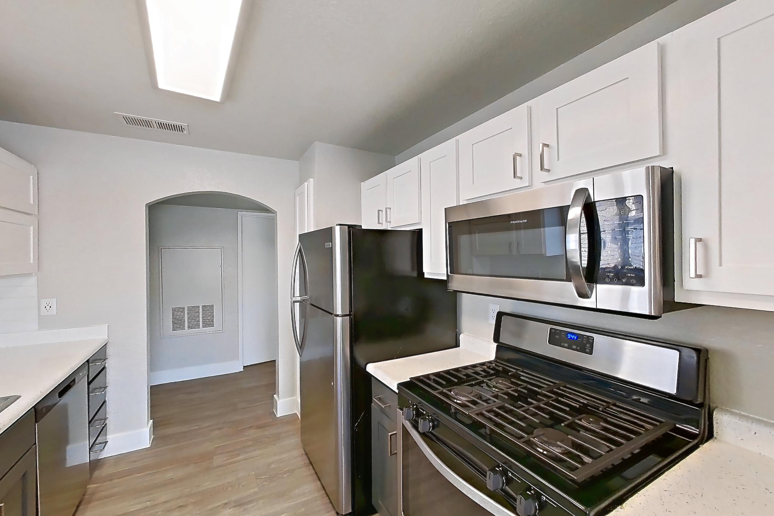 Kitchen with gas range, light countertops, light stone countertops, light wood-finish flooring, microwave, oven/range, refrigerator, and stainless steel appliances, Apartment 2146 at Vintage Pointe