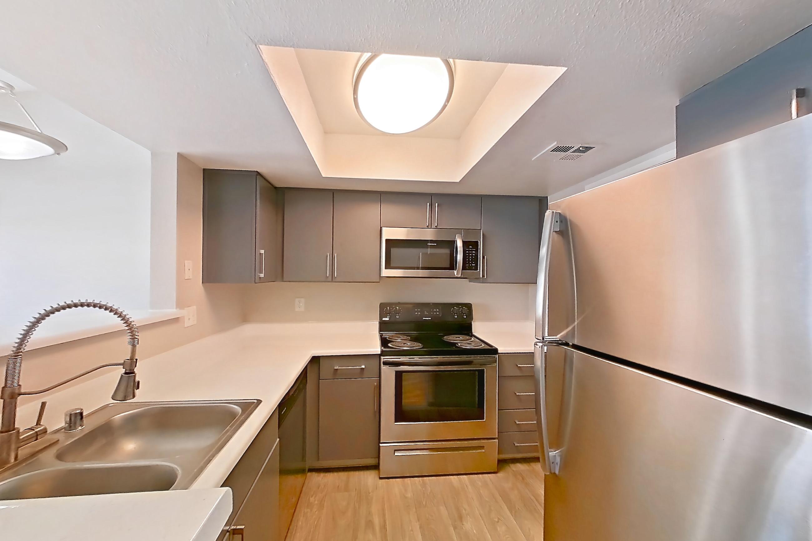 Kitchen with dishwasher, electric range, fireplace, light countertops, light stone countertops, light wood-finish flooring, microwave, oven/range, refrigerator, stainless steel appliances, and tile fireplace, Apartment 2233 at The Met Las Vegas