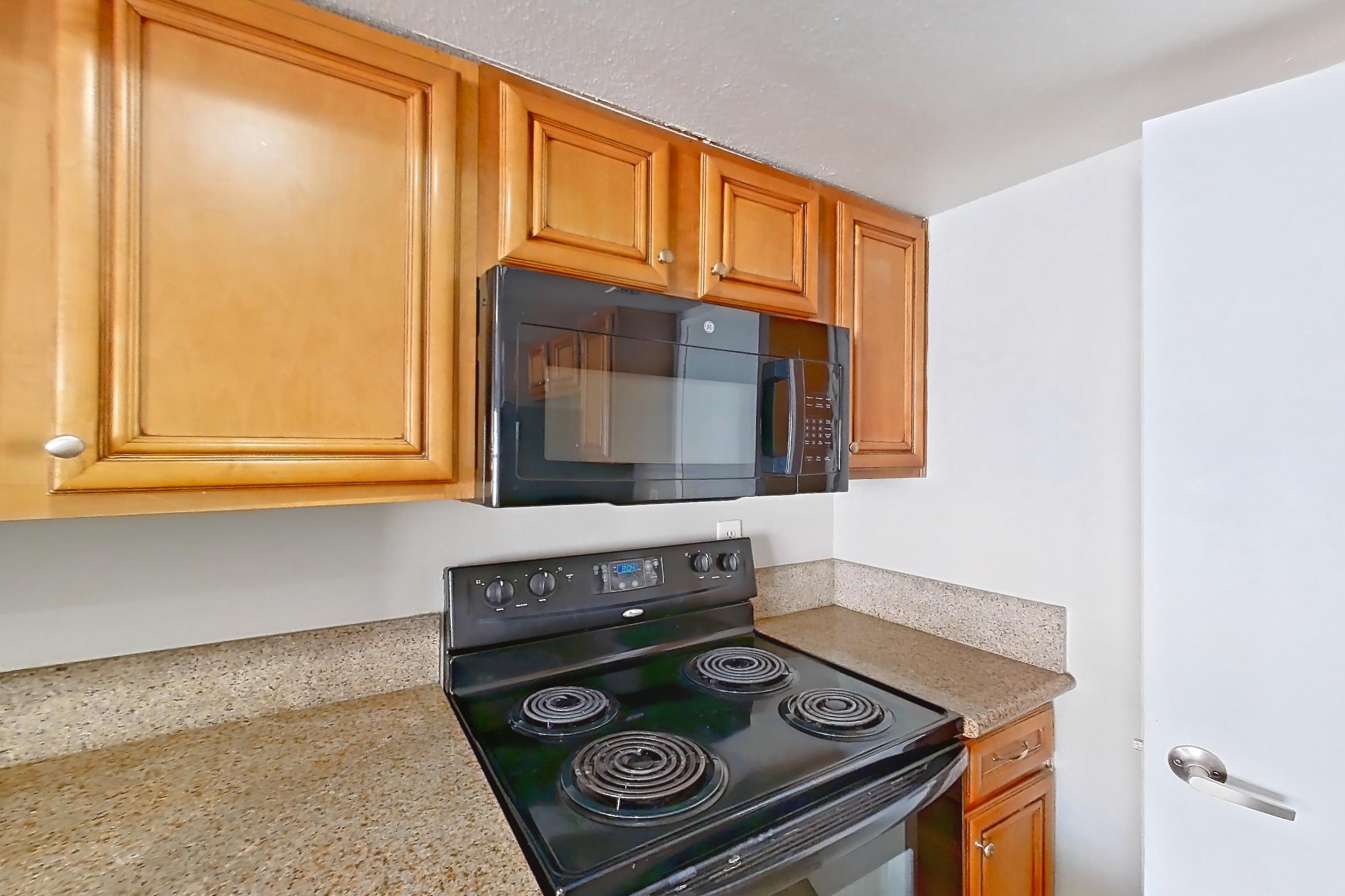 Kitchen with black appliances, dishwasher, electric range, light countertops, light stone countertops, light wood-finish flooring, microwave, oven/range, and refrigerator, Apartment 2171 at The Met Las Vegas