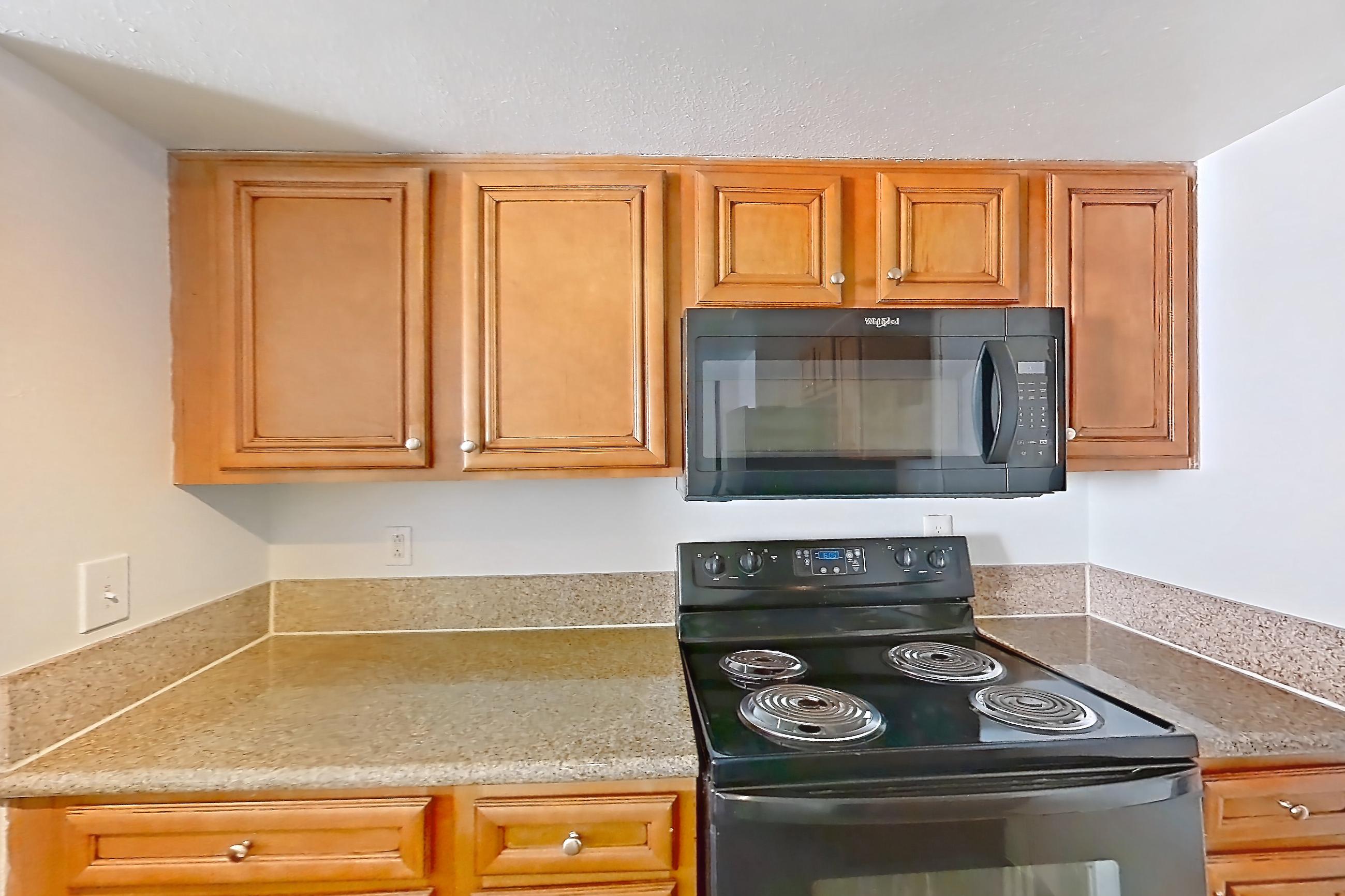Kitchen with black appliances, dishwasher, electric range, fireplace, light countertops, light stone countertops, light wood-finish flooring, oven/range, and refrigerator, Apartment 2175 at The Met Las Vegas