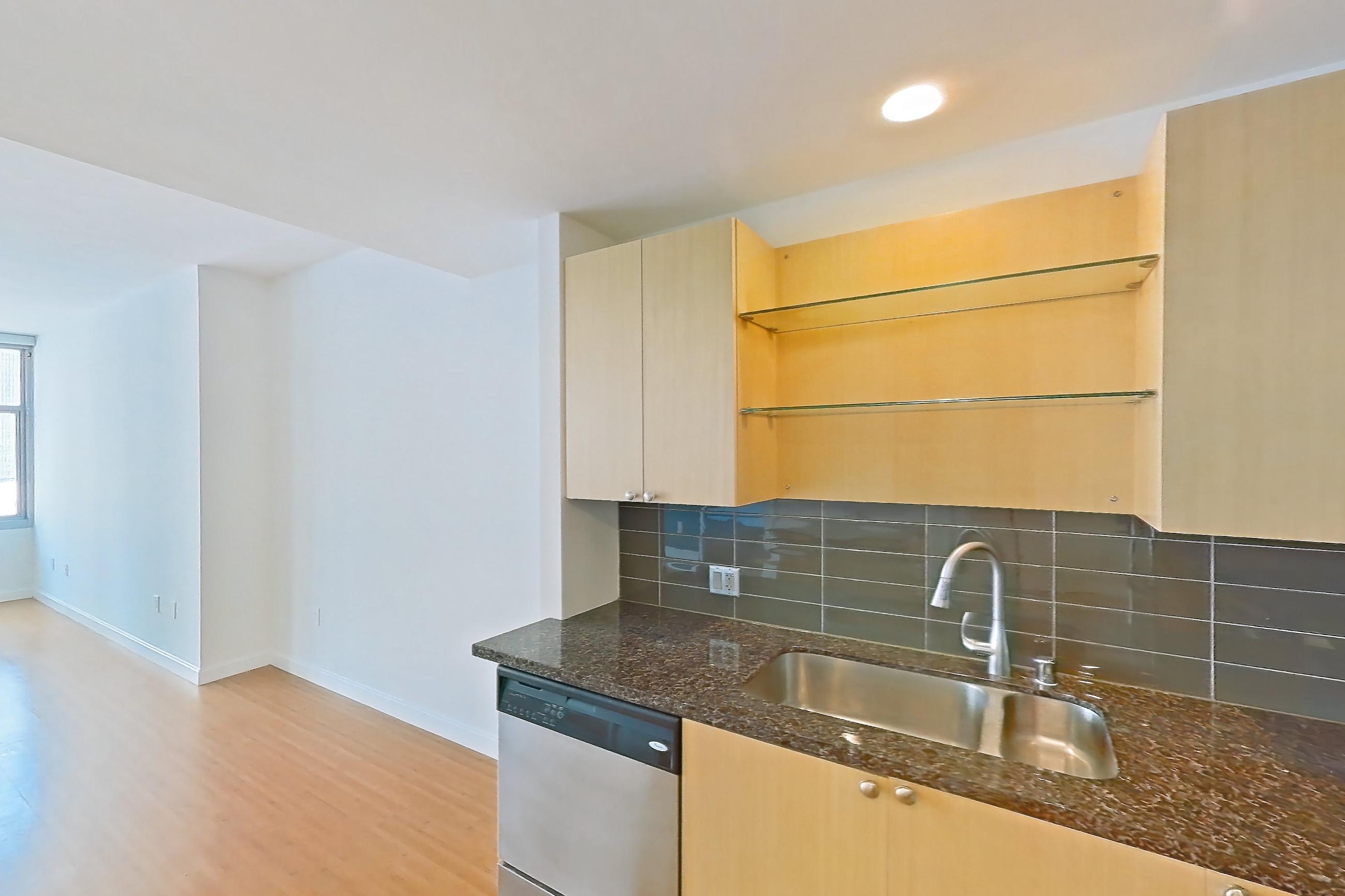 Kitchen with dark stone countertops, dishwasher, light wood-finish flooring, oven/range, refrigerator, and stainless steel appliances, Apartment E-1354 at The Element