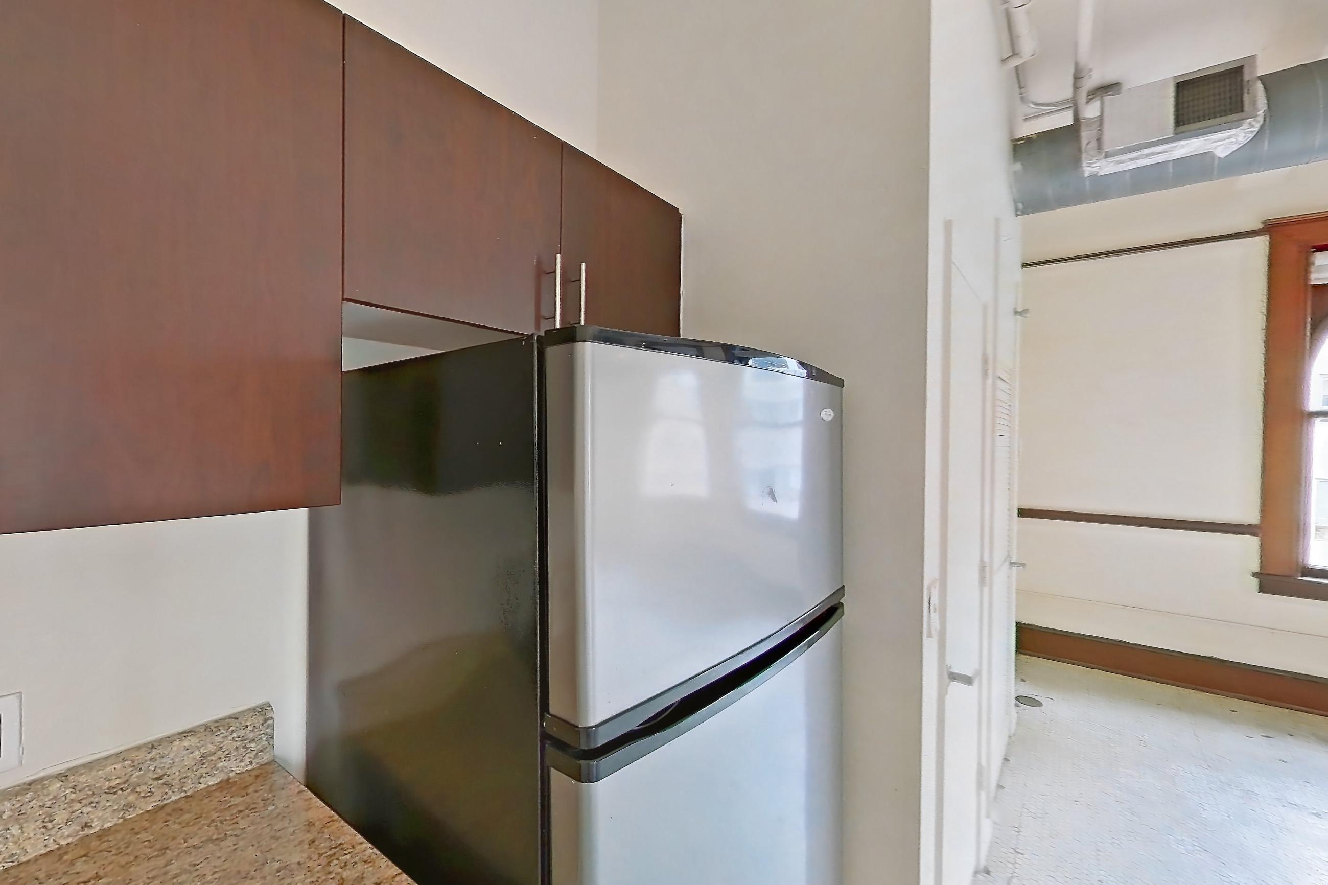 Kitchen with dishwasher, electric range, light countertops, light stone countertops, light vinyl flooring, oven/range, refrigerator, stainless steel appliances, and vinyl tile flooring, Apartment W-0702 at The Wilson