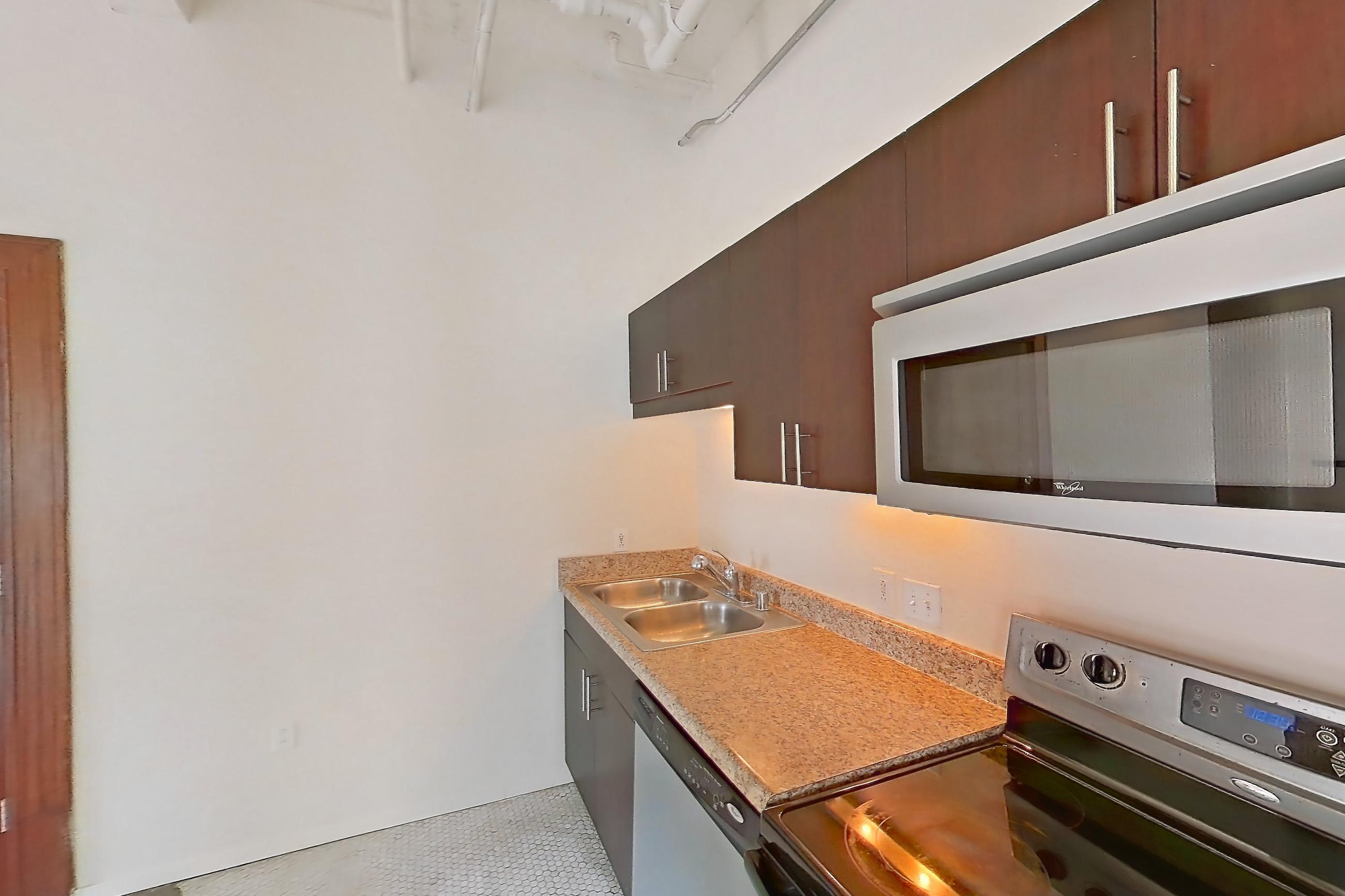 Kitchen with dishwasher, electric range, light countertops, light stone countertops, light vinyl flooring, oven/range, refrigerator, stainless steel appliances, and vinyl tile flooring, Apartment W-0702 at The Wilson