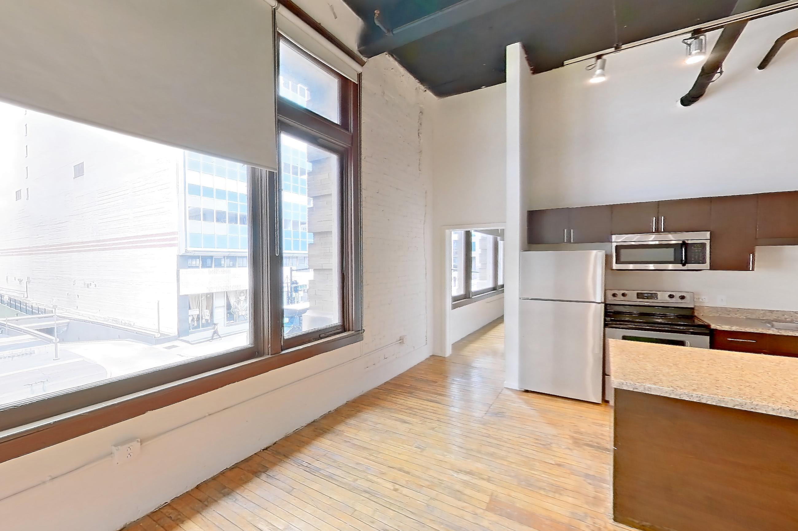 Living room with dishwasher, electric range, light countertops, light wood-finish flooring, oven/range, refrigerator, stainless steel appliances, and wood-finish flooring, Apartment W-0206 at The Wilson