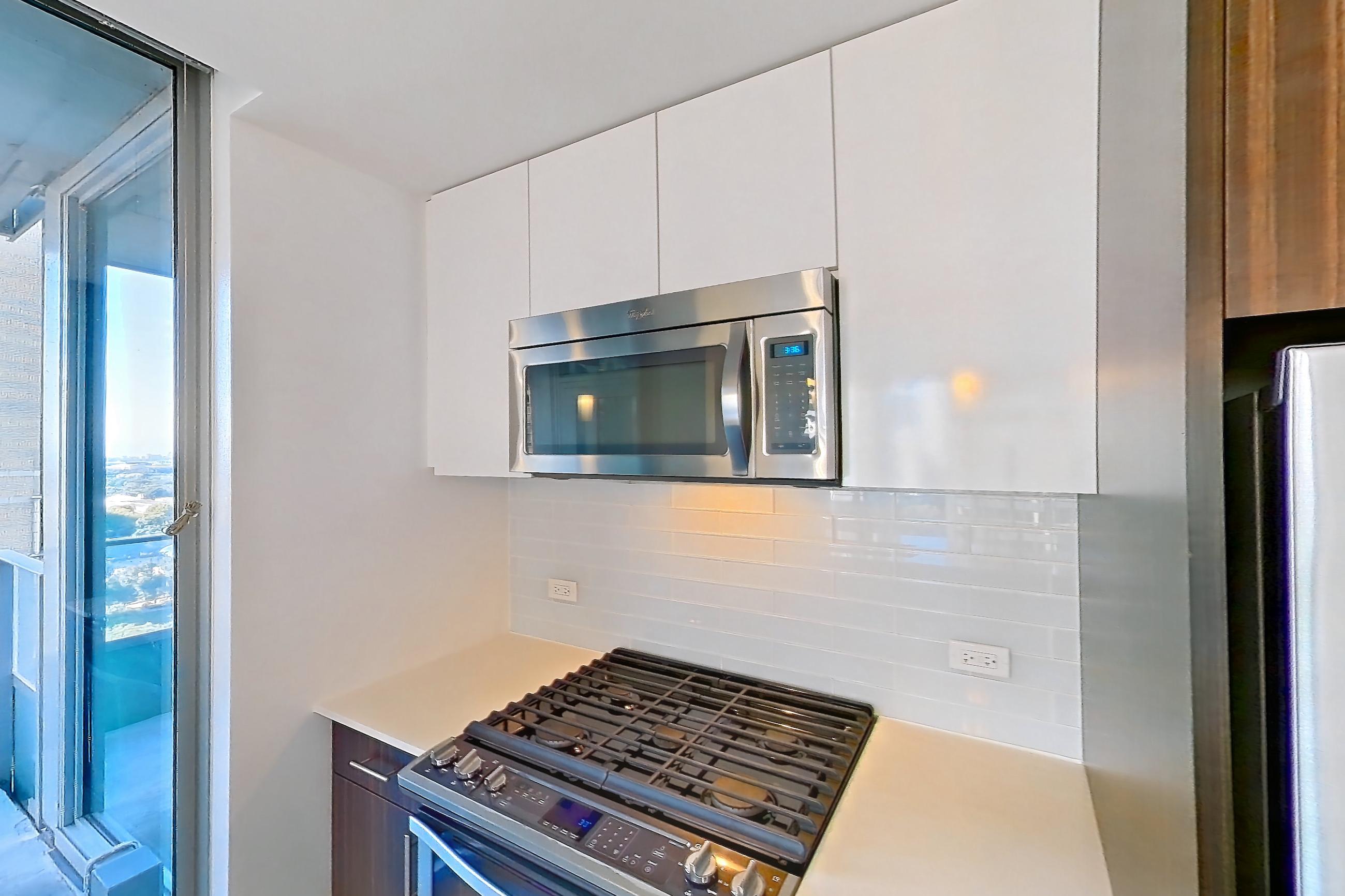 Kitchen with dishwasher, gas range, light countertops, light stone countertops, light wood-finish flooring, microwave, oven/range, refrigerator, and stainless steel appliances, Apartment 2207 at Mila