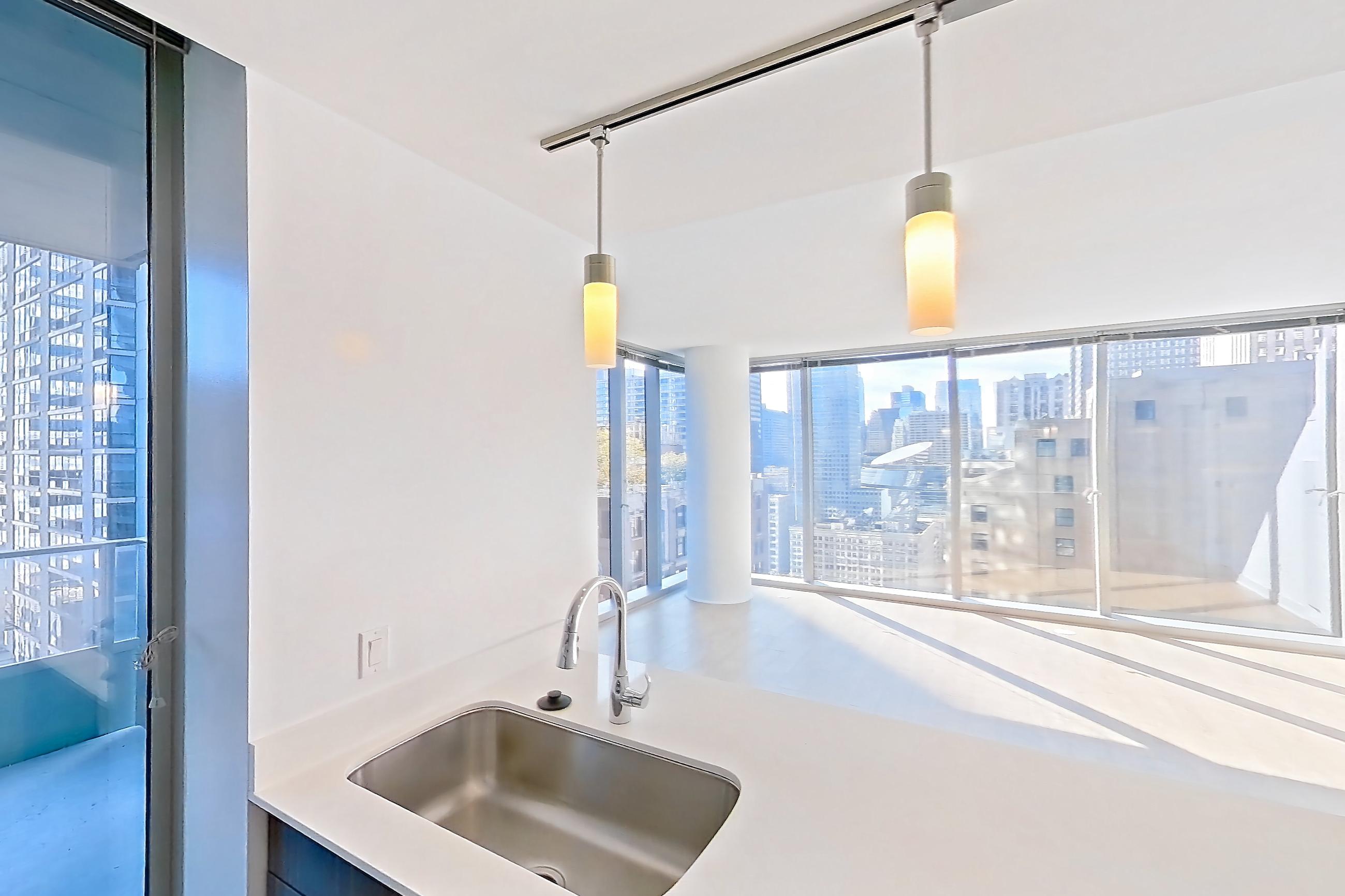 Kitchen with dishwasher, gas range, light countertops, light stone countertops, light wood-finish flooring, microwave, oven/range, refrigerator, skyline view, and stainless steel appliances, Apartment 2810 at Mila