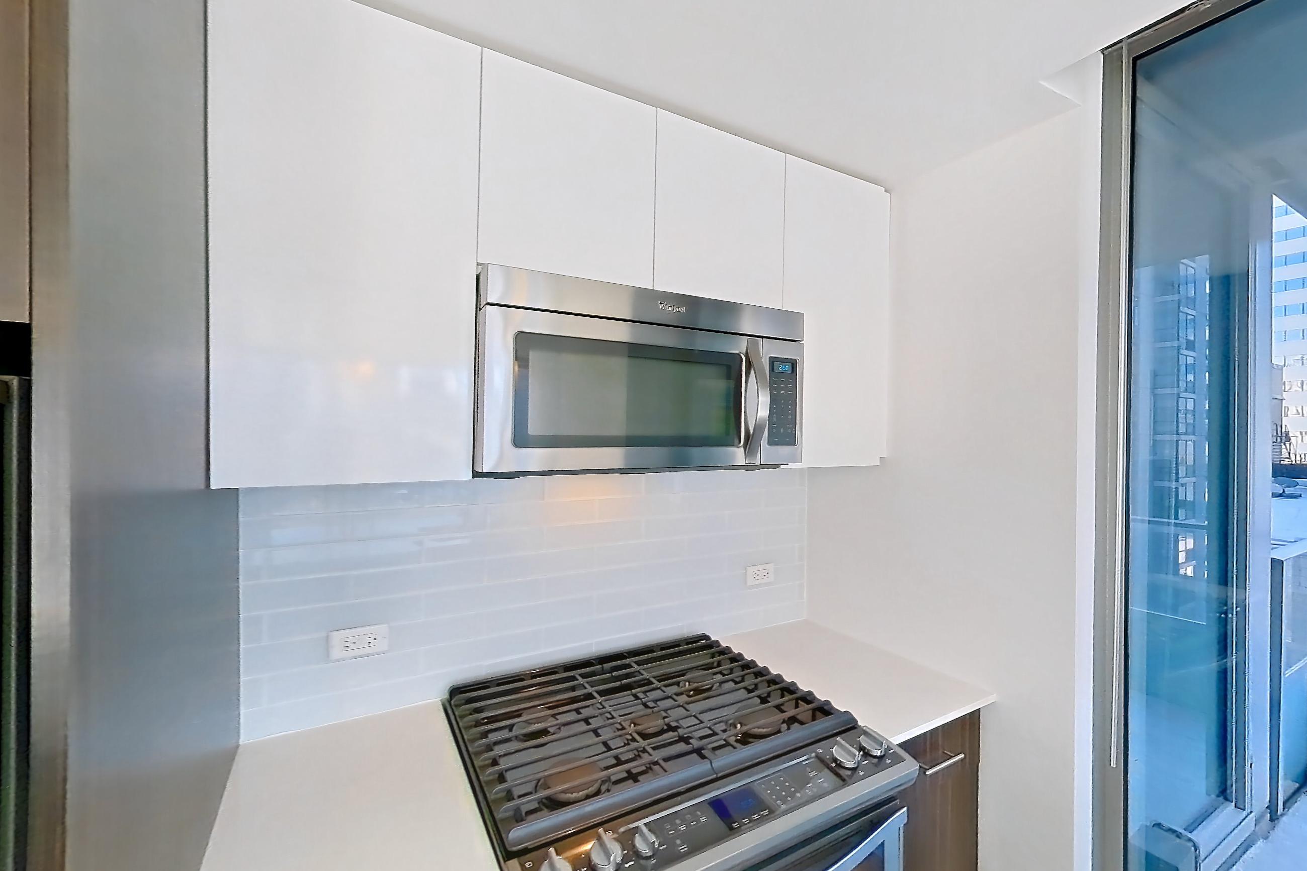 Kitchen with dishwasher, gas range, light countertops, light stone countertops, light wood-finish flooring, microwave, oven/range, refrigerator, skyline view, and stainless steel appliances, Apartment 2810 at Mila
