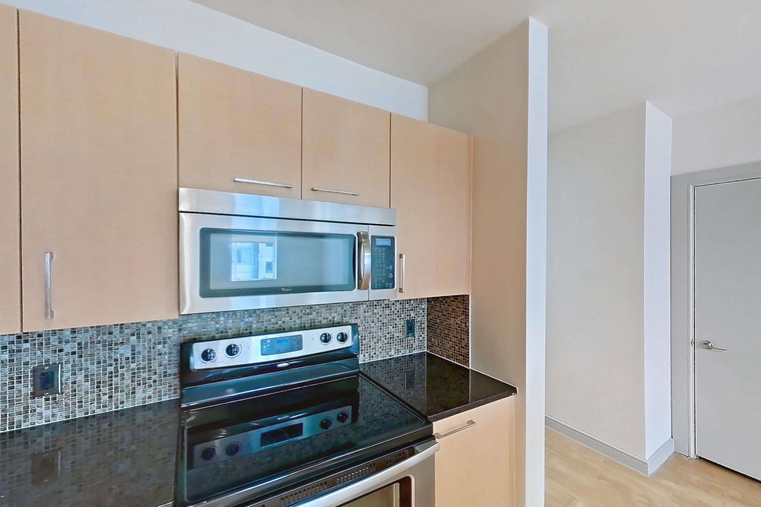 Kitchen with dark stone countertops, dishwasher, electric range, light countertops, light wood-finish flooring, microwave, oven/range, refrigerator, stainless steel appliances, and white appliances, Apartment C-0611 at The Continental