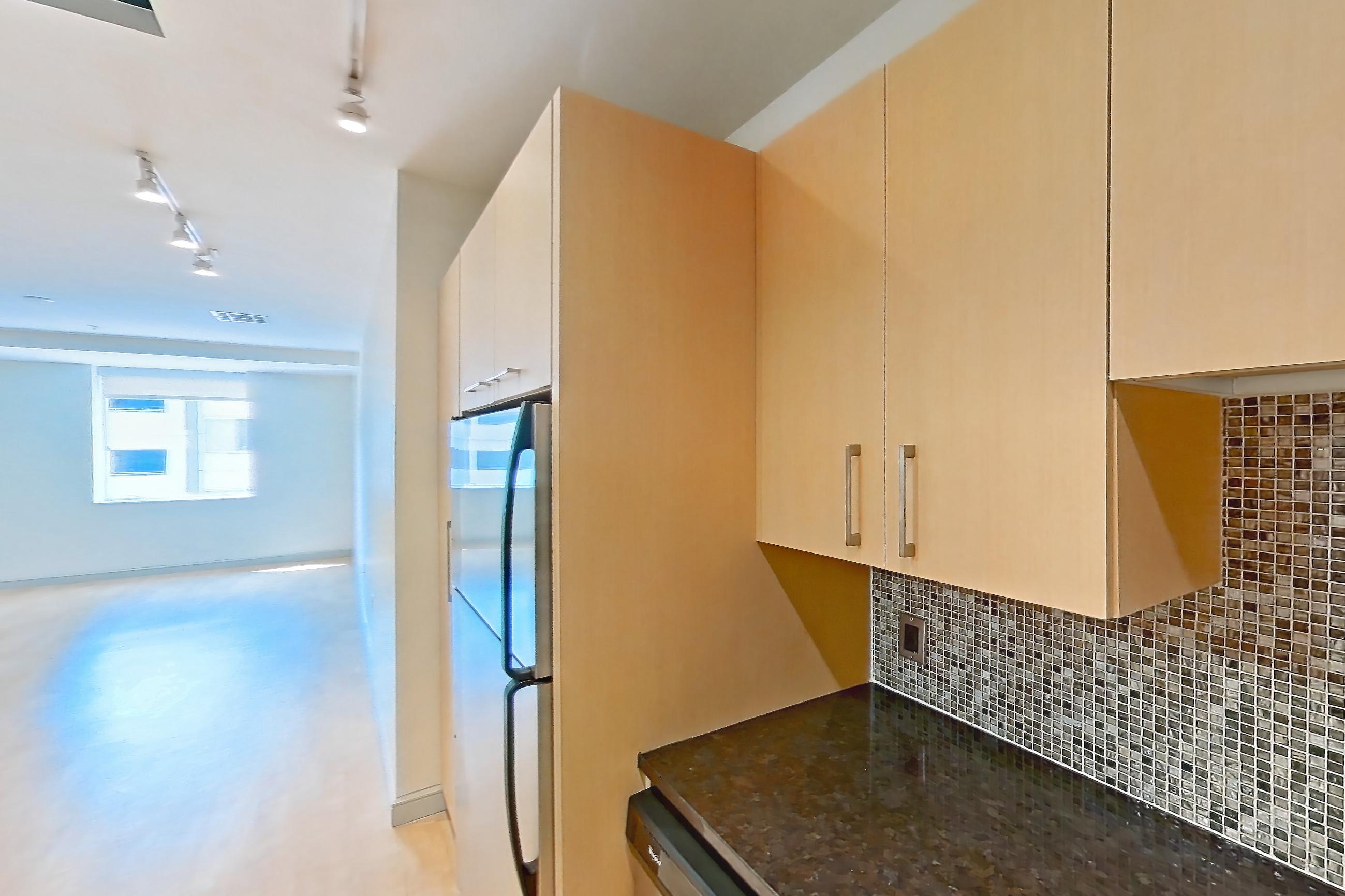 Kitchen with dark stone countertops, dishwasher, electric range, light countertops, light wood-finish flooring, microwave, oven/range, refrigerator, stainless steel appliances, and white appliances, Apartment C-0611 at The Continental
