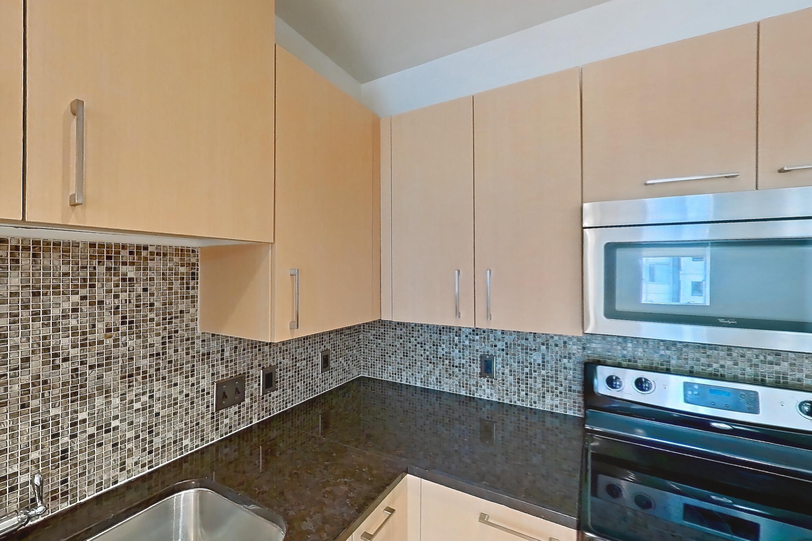 Kitchen with dark stone countertops, dishwasher, electric range, light countertops, light wood-finish flooring, microwave, oven/range, refrigerator, stainless steel appliances, and white appliances, Apartment C-0611 at The Continental