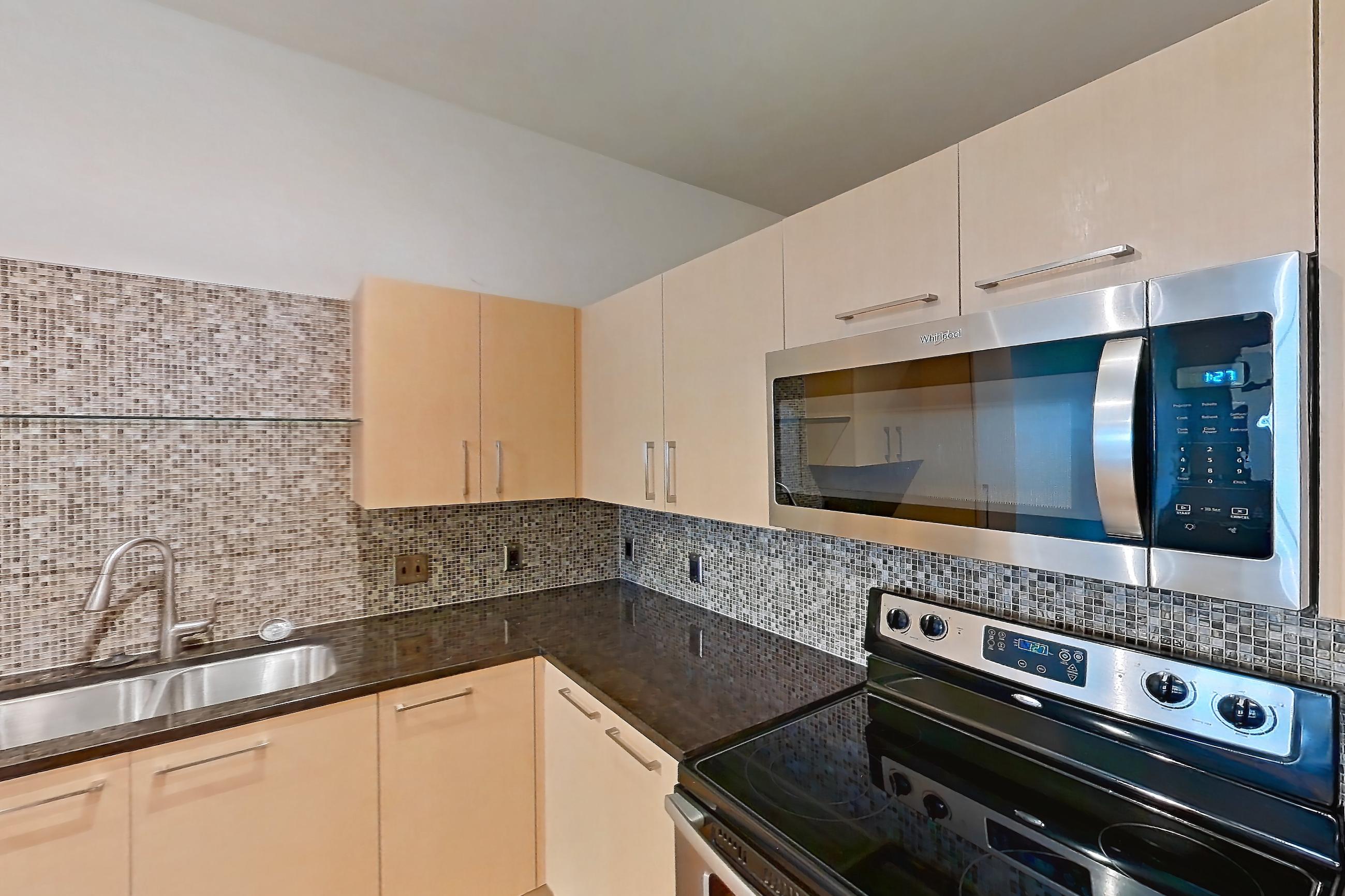 Kitchen with dark stone countertops, dishwasher, electric range, light wood-finish flooring, microwave, oven/range, refrigerator, and stainless steel appliances, Apartment C-0214 at The Continental