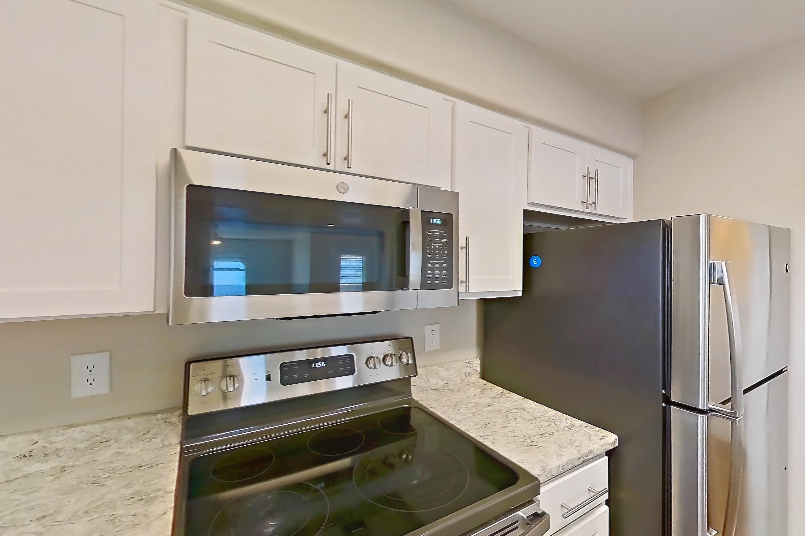 Kitchen with dishwasher, electric range, light countertops, light stone countertops, light wood-finish flooring, microwave, oven/range, refrigerator, and stainless steel appliances, Apartment 3184 at San Valiente