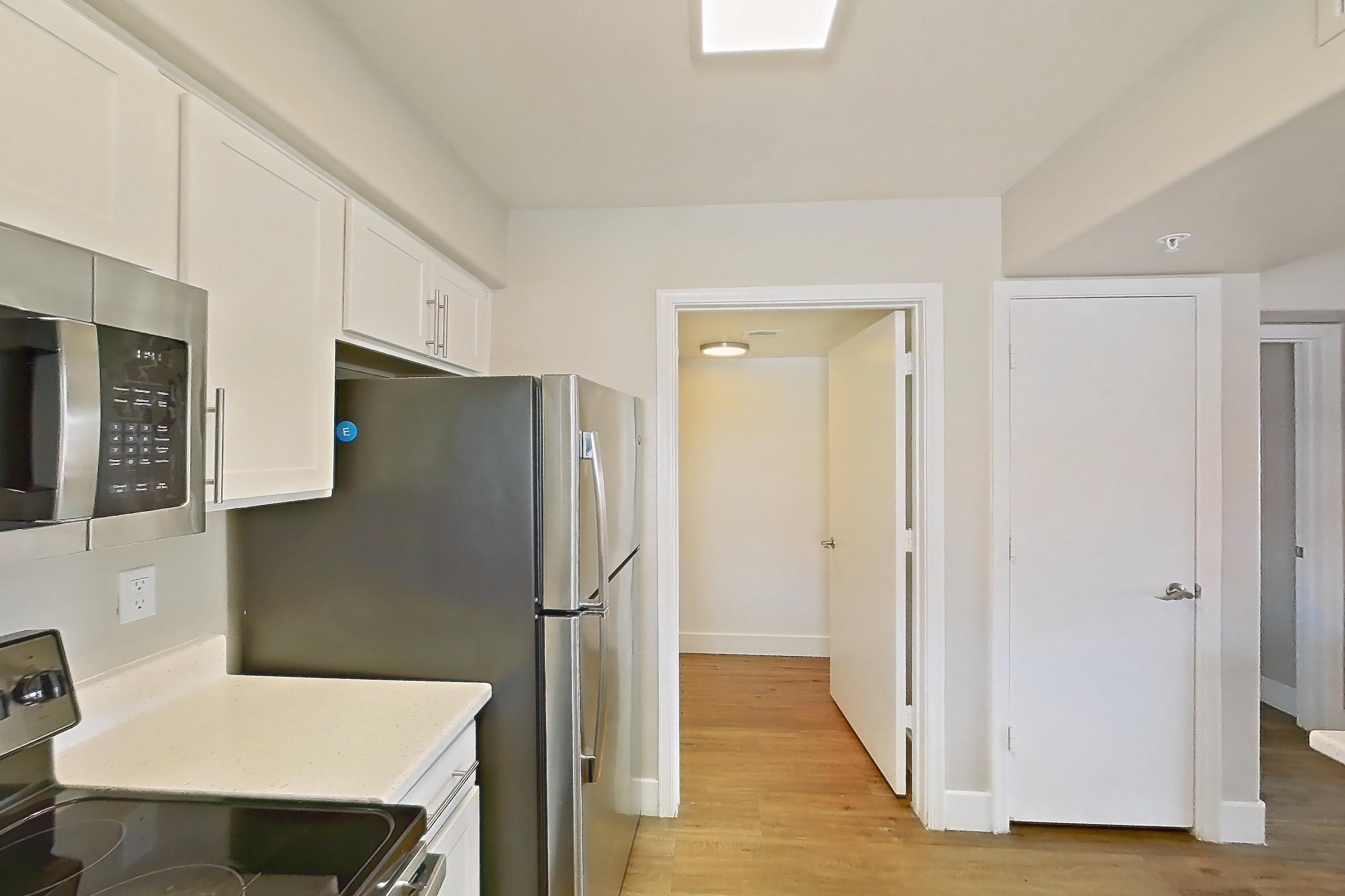 Kitchen with dishwasher, electric range, light countertops, light stone countertops, light wood-finish flooring, microwave, oven/range, refrigerator, stainless steel appliances, and white appliances, Apartment 3190 at San Valiente