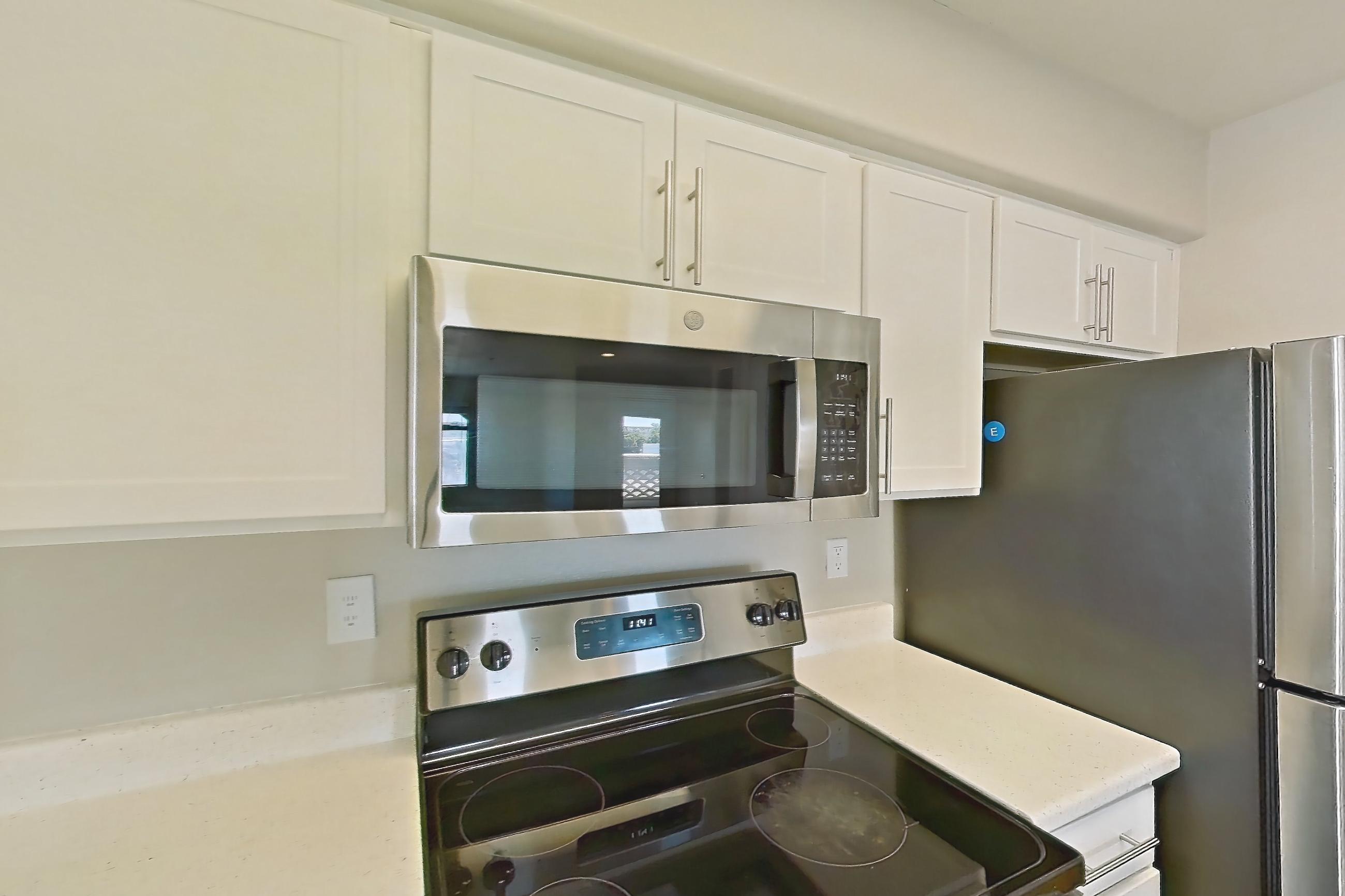 Kitchen with dishwasher, electric range, light countertops, light stone countertops, light wood-finish flooring, microwave, oven/range, refrigerator, stainless steel appliances, and white appliances, Apartment 3190 at San Valiente