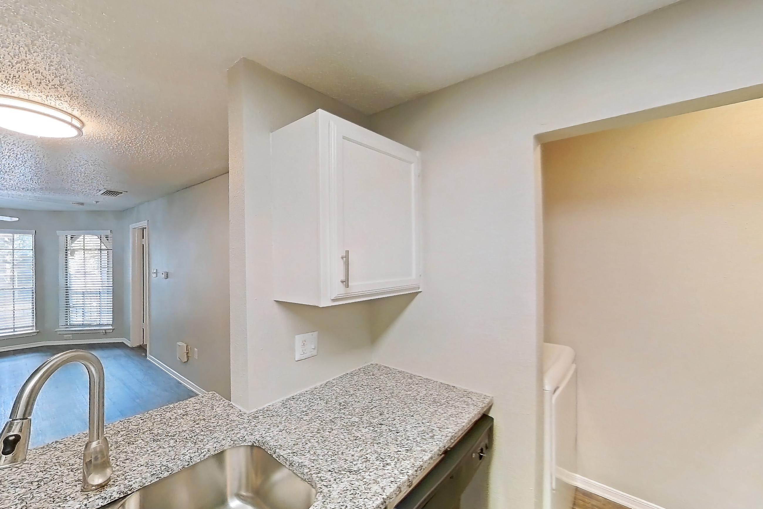 Kitchen with black appliances, brick fireplace, dark wood-finish flooring, dishwasher, electric range, fireplace, light stone countertops, light wood-finish flooring, oven/range, refrigerator, and stainless steel appliances, Apartment 03-0327 at The Arbors of Las Colinas