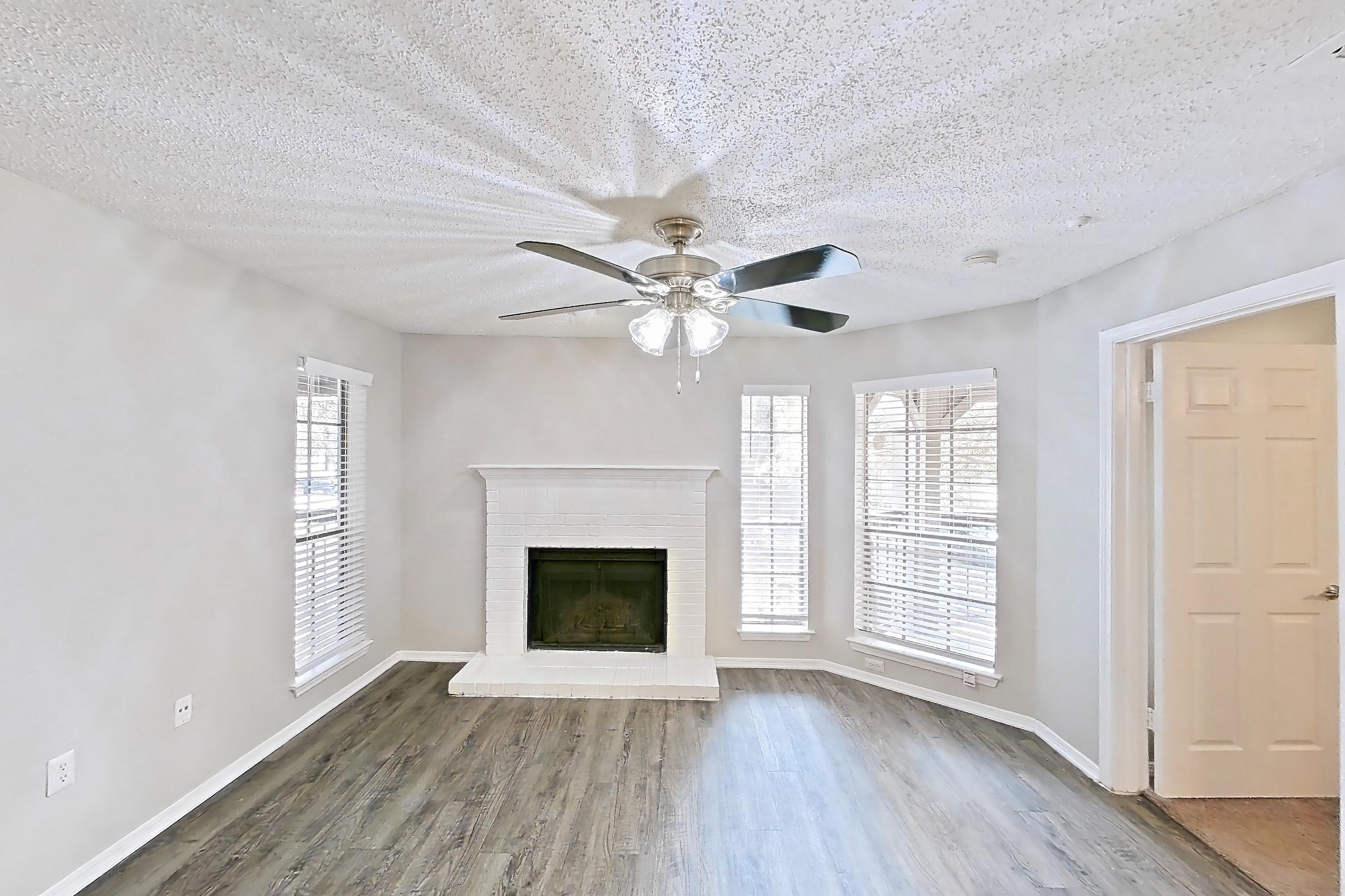 Living room with brick fireplace, dark wood-finish flooring, and fireplace, Apartment 03-0327 at The Arbors of Las Colinas
