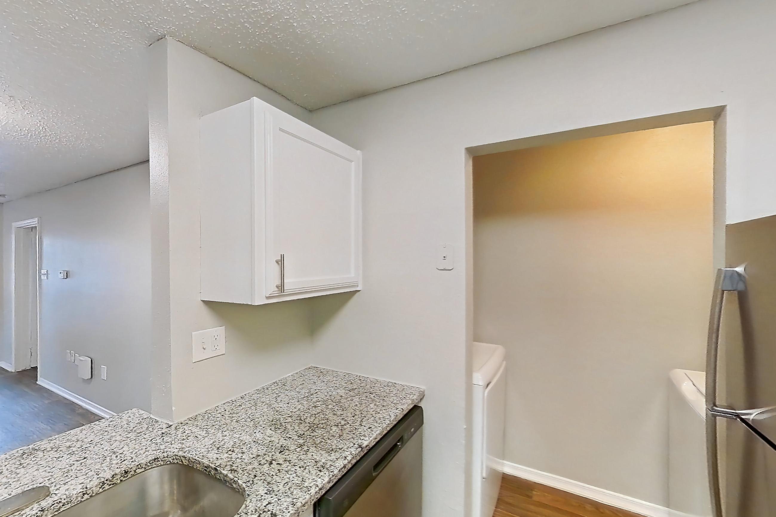 Kitchen with dark wood-finish flooring, dishwasher, electric range, fireplace, light stone countertops, light wood-finish flooring, oven/range, refrigerator, and stainless steel appliances, Apartment 11-1117 at The Arbors of Las Colinas