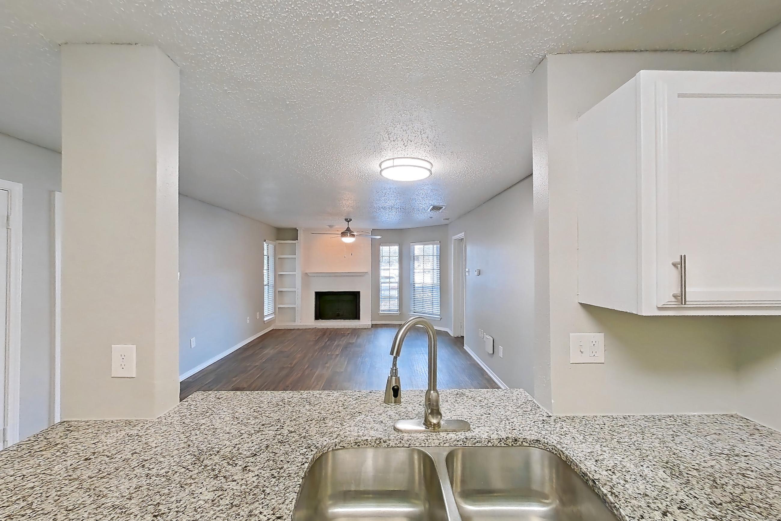 Kitchen with dark wood-finish flooring, dishwasher, electric range, fireplace, light stone countertops, light wood-finish flooring, oven/range, refrigerator, and stainless steel appliances, Apartment 11-1117 at The Arbors of Las Colinas