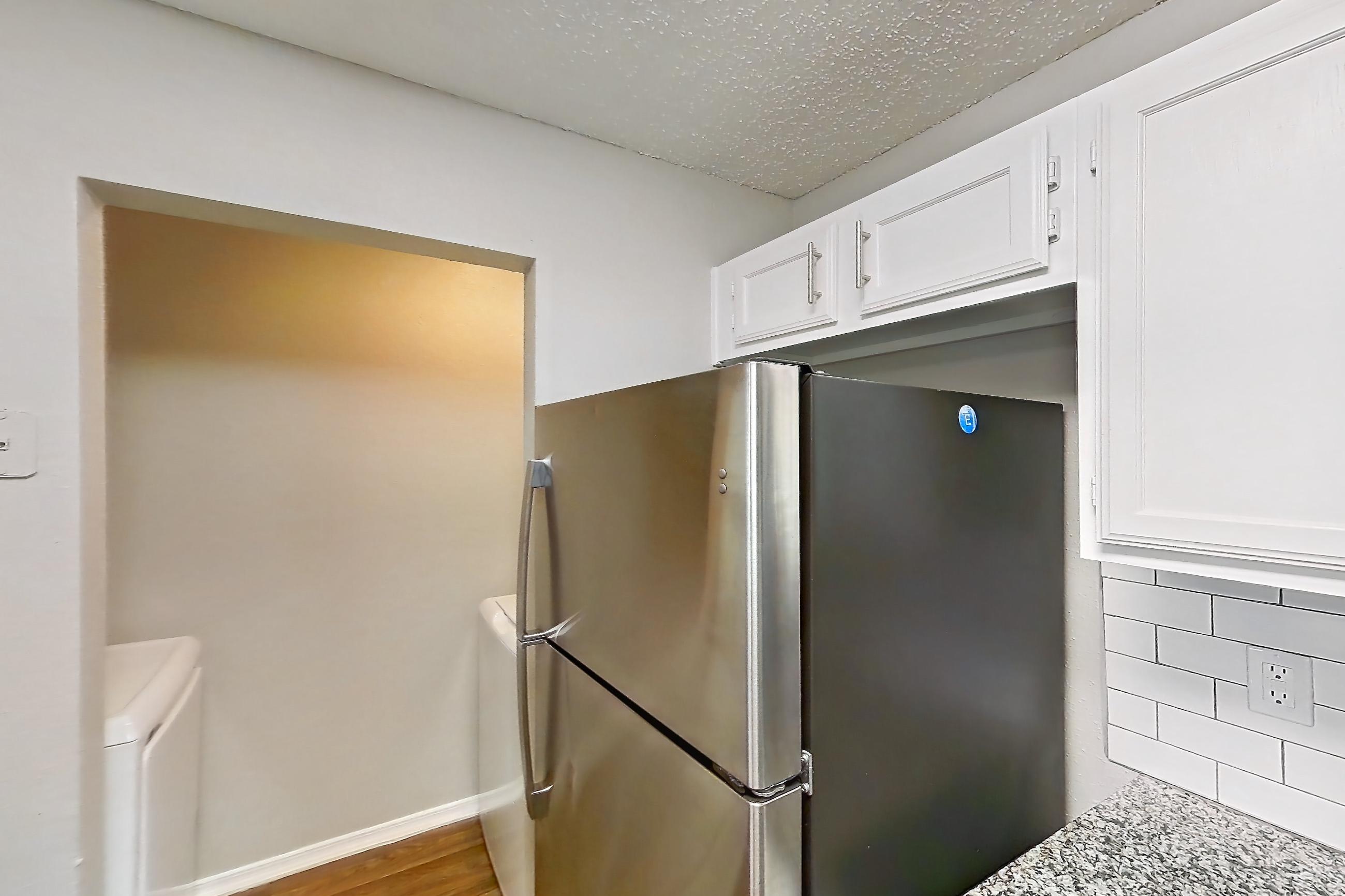 Kitchen with dark wood-finish flooring, dishwasher, electric range, fireplace, light stone countertops, light wood-finish flooring, oven/range, refrigerator, and stainless steel appliances, Apartment 11-1117 at The Arbors of Las Colinas