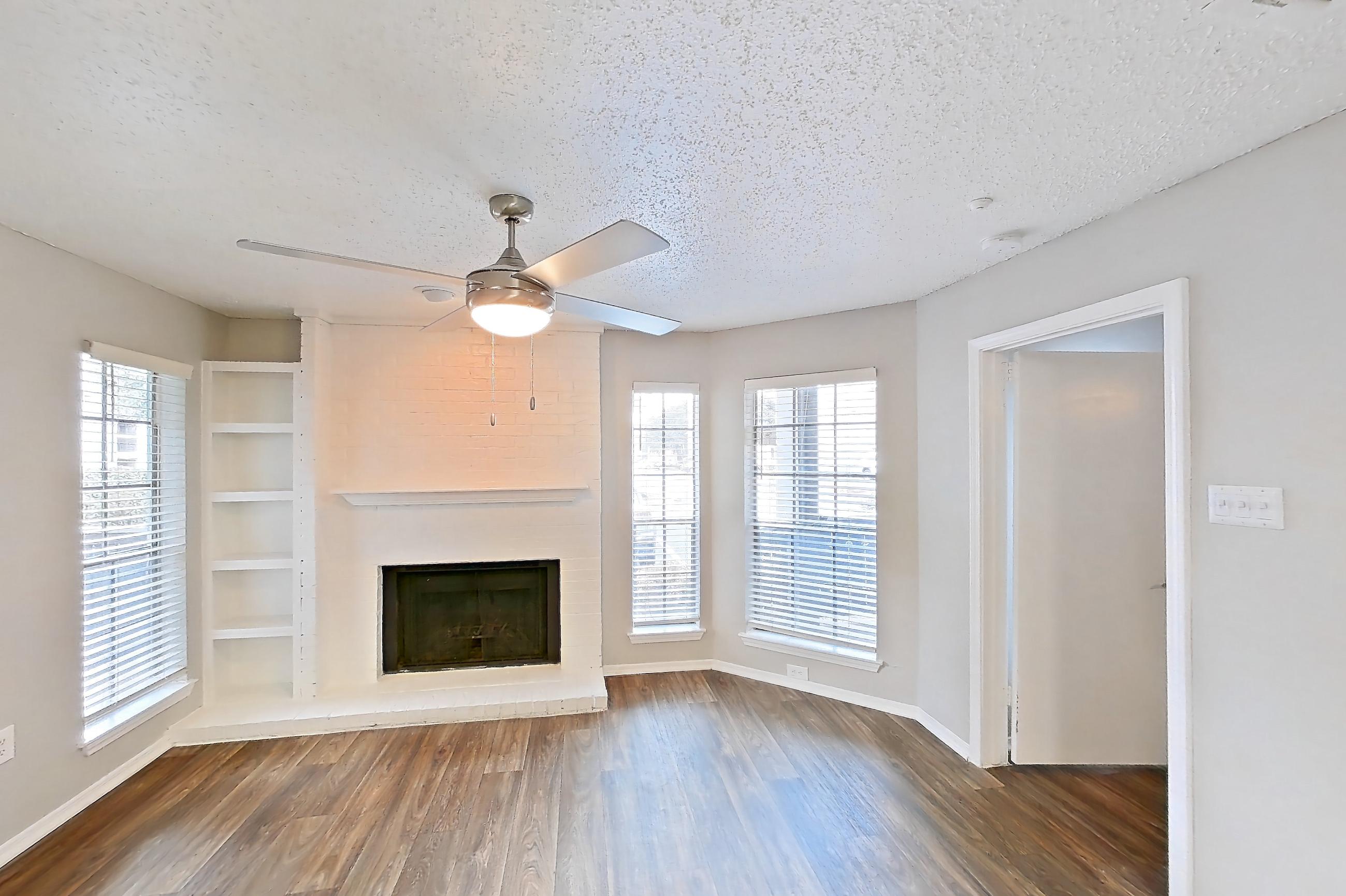Living room with brick fireplace, dark wood-finish flooring, and fireplace, Apartment 11-1117 at The Arbors of Las Colinas