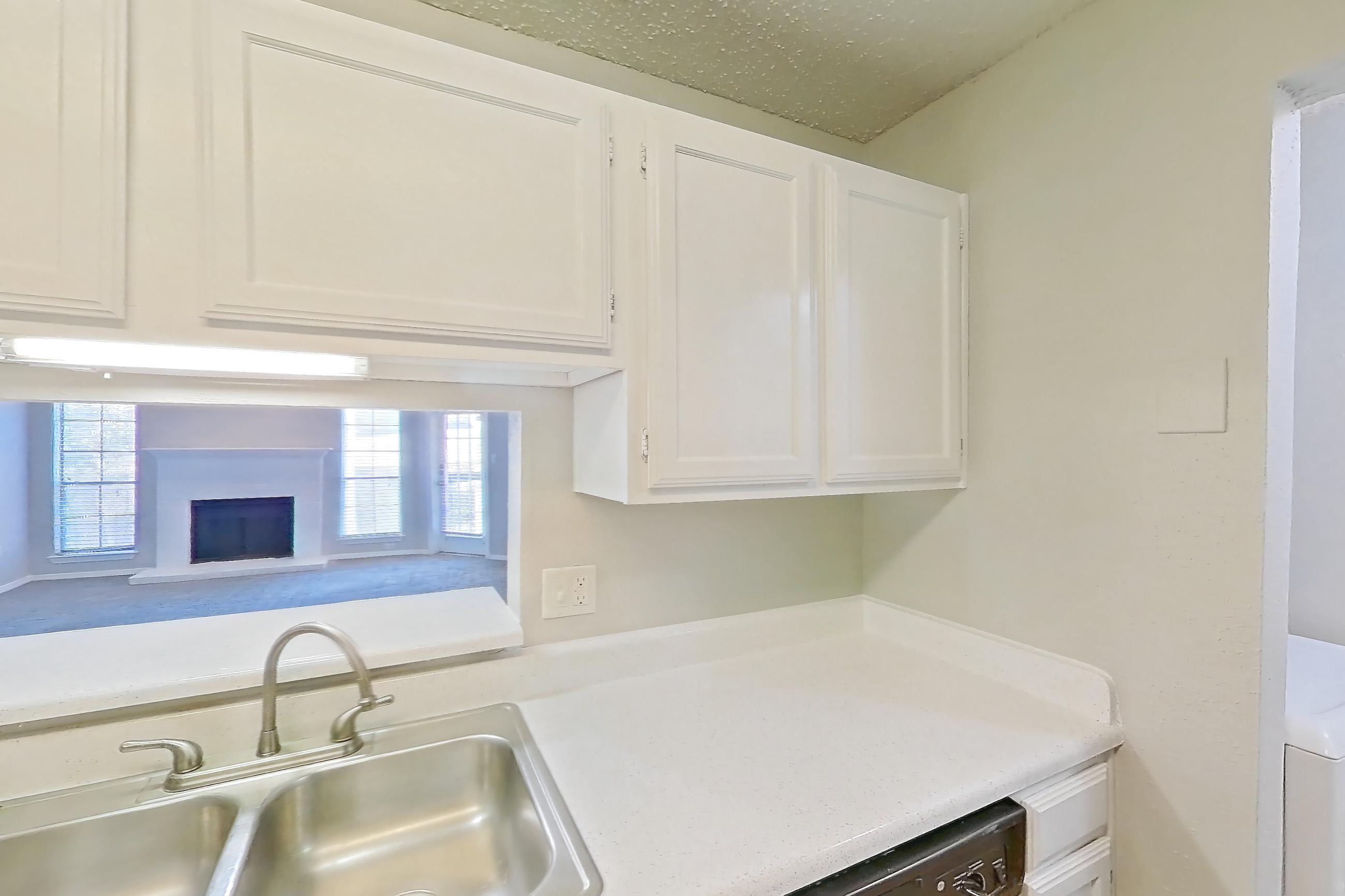 Kitchen with black appliances, dishwasher, electric range, fireplace, light countertops, light wood-finish flooring, microwave, oven/range, range hood, refrigerator, stainless steel appliances, and wood-finish flooring, Apartment 08-0821 at The Arbors of Las Colinas