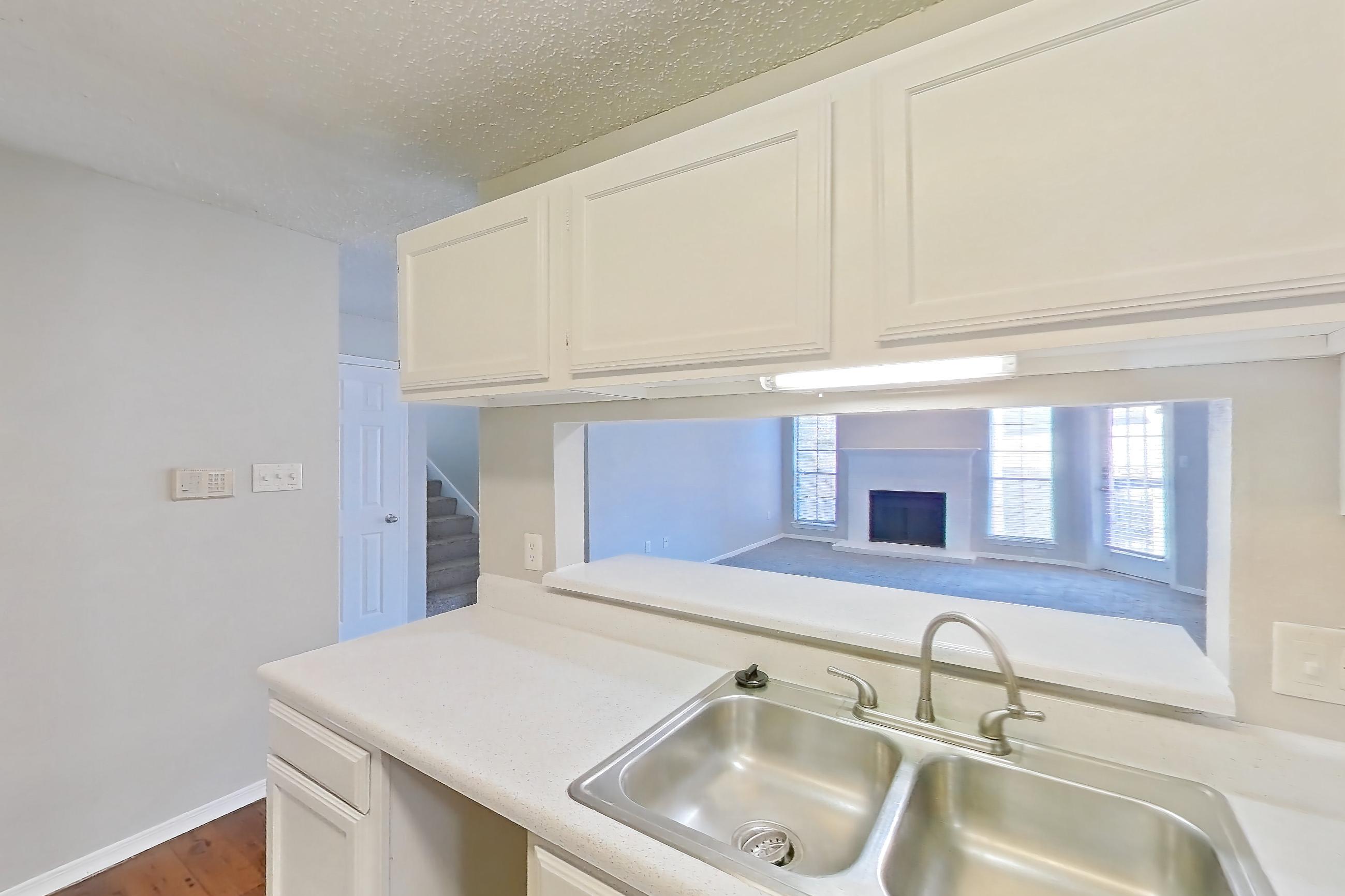Kitchen with black appliances, dishwasher, electric range, fireplace, light countertops, light wood-finish flooring, microwave, oven/range, range hood, refrigerator, stainless steel appliances, and wood-finish flooring, Apartment 08-0821 at The Arbors of Las Colinas