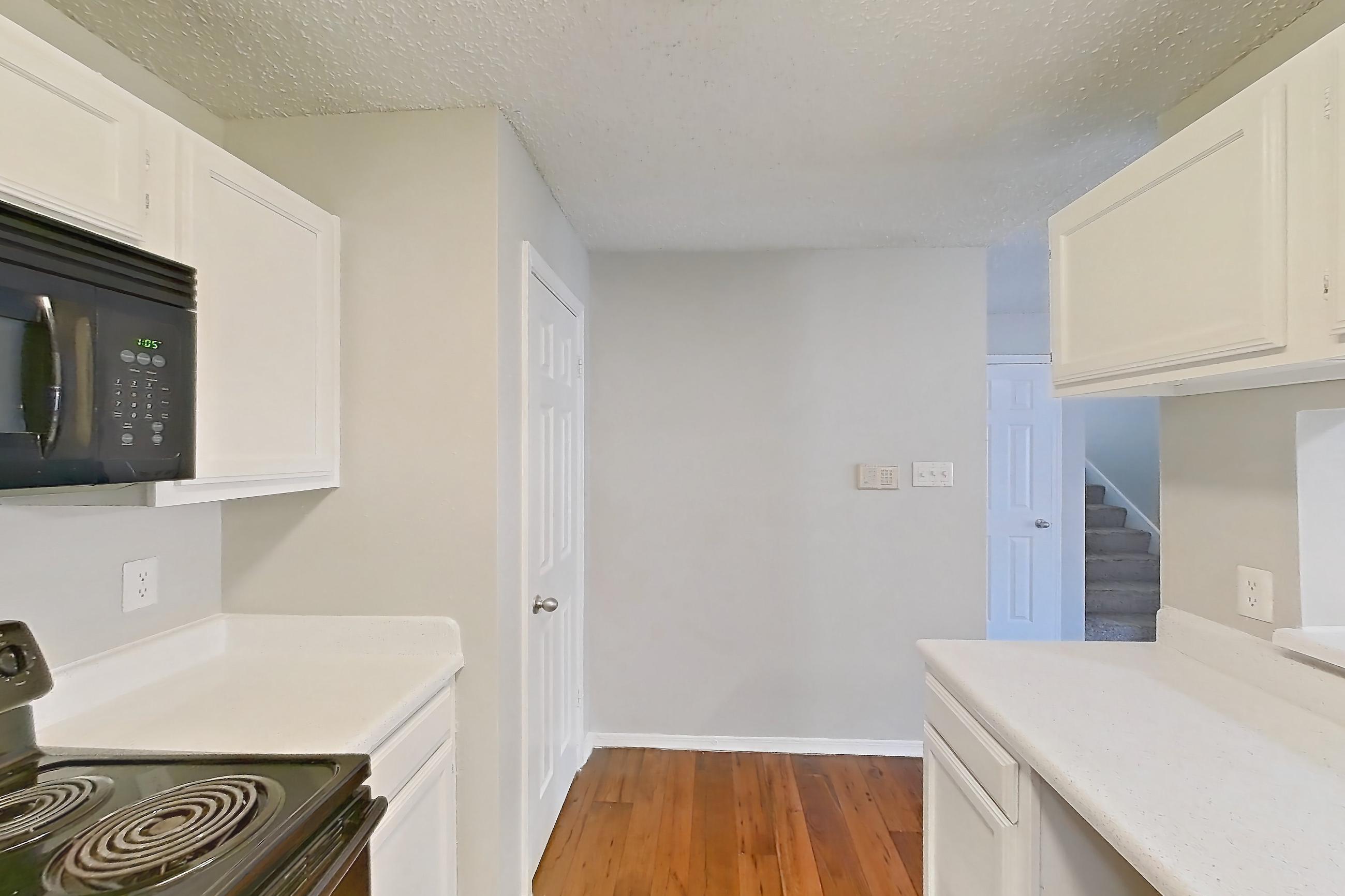 Kitchen with black appliances, dishwasher, electric range, fireplace, light countertops, light wood-finish flooring, microwave, oven/range, range hood, refrigerator, stainless steel appliances, and wood-finish flooring, Apartment 08-0821 at The Arbors of Las Colinas