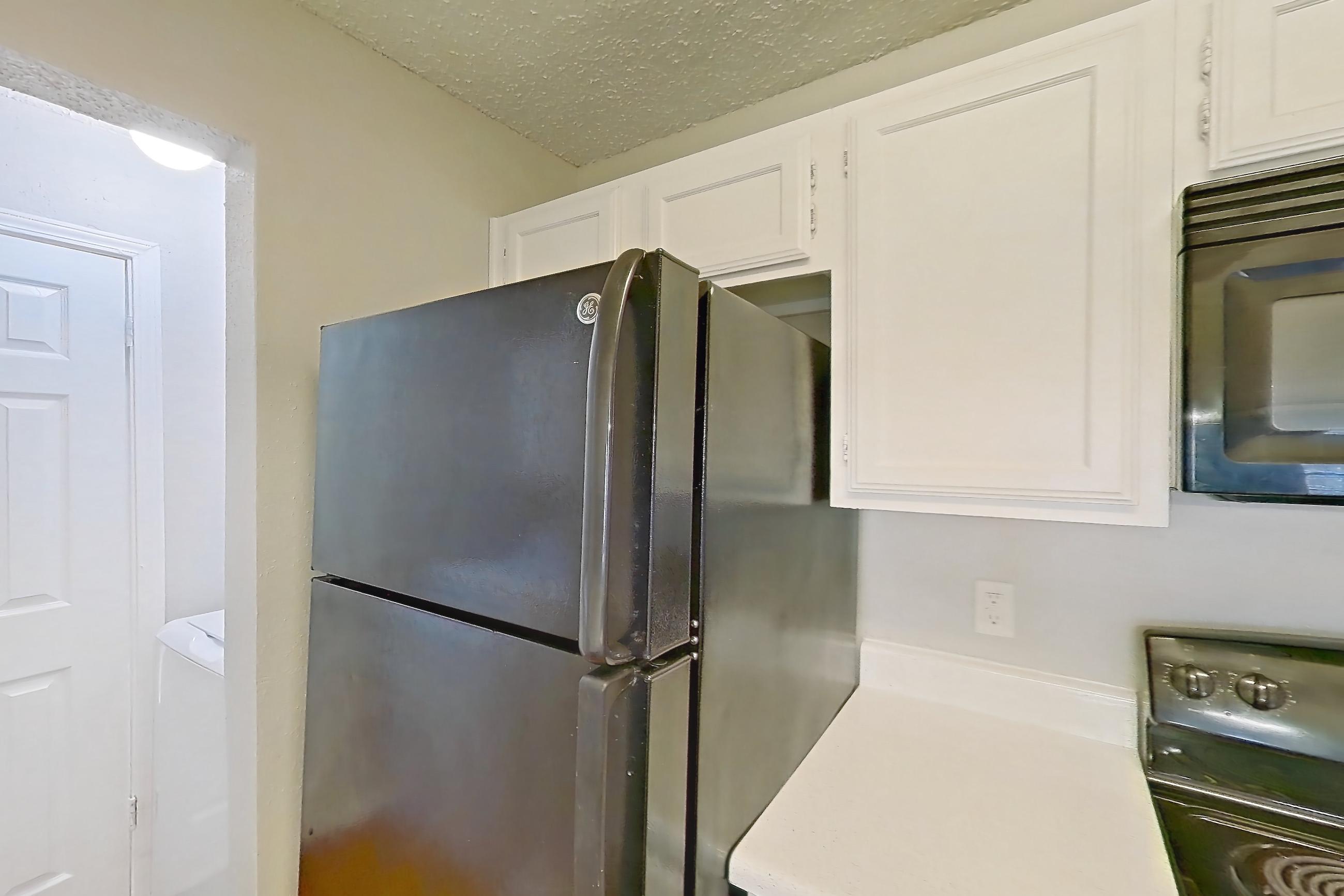Kitchen with black appliances, dishwasher, electric range, fireplace, light countertops, light wood-finish flooring, microwave, oven/range, range hood, refrigerator, stainless steel appliances, and wood-finish flooring, Apartment 08-0821 at The Arbors of Las Colinas