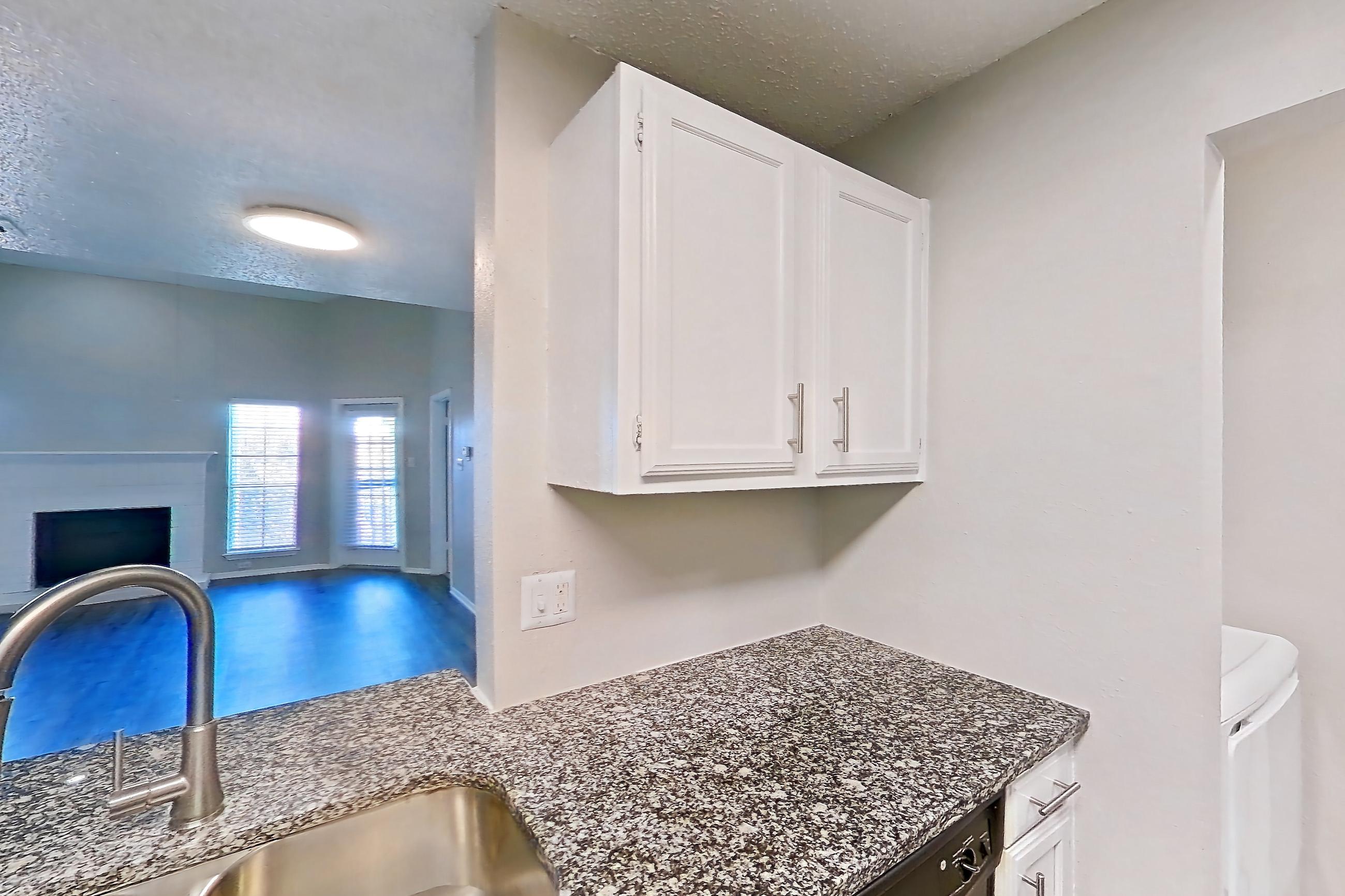 Kitchen with black appliances, dark stone countertops, dishwasher, electric range, light countertops, light wood-finish flooring, microwave, oven/range, refrigerator, and stainless steel appliances, Apartment 05-0521 at The Arbors of Las Colinas