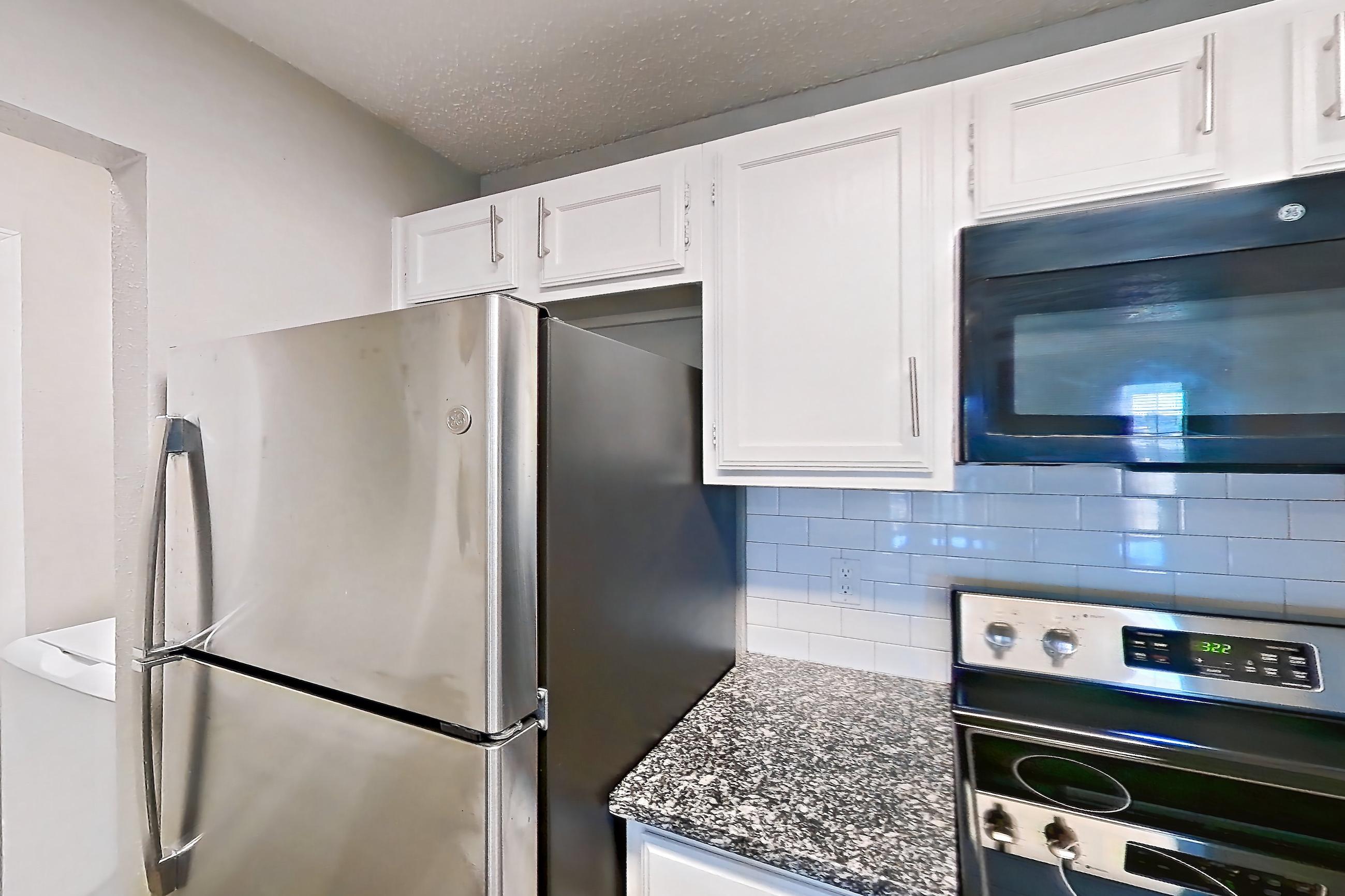 Kitchen with black appliances, dark stone countertops, dishwasher, electric range, light countertops, light wood-finish flooring, microwave, oven/range, refrigerator, and stainless steel appliances, Apartment 05-0521 at The Arbors of Las Colinas