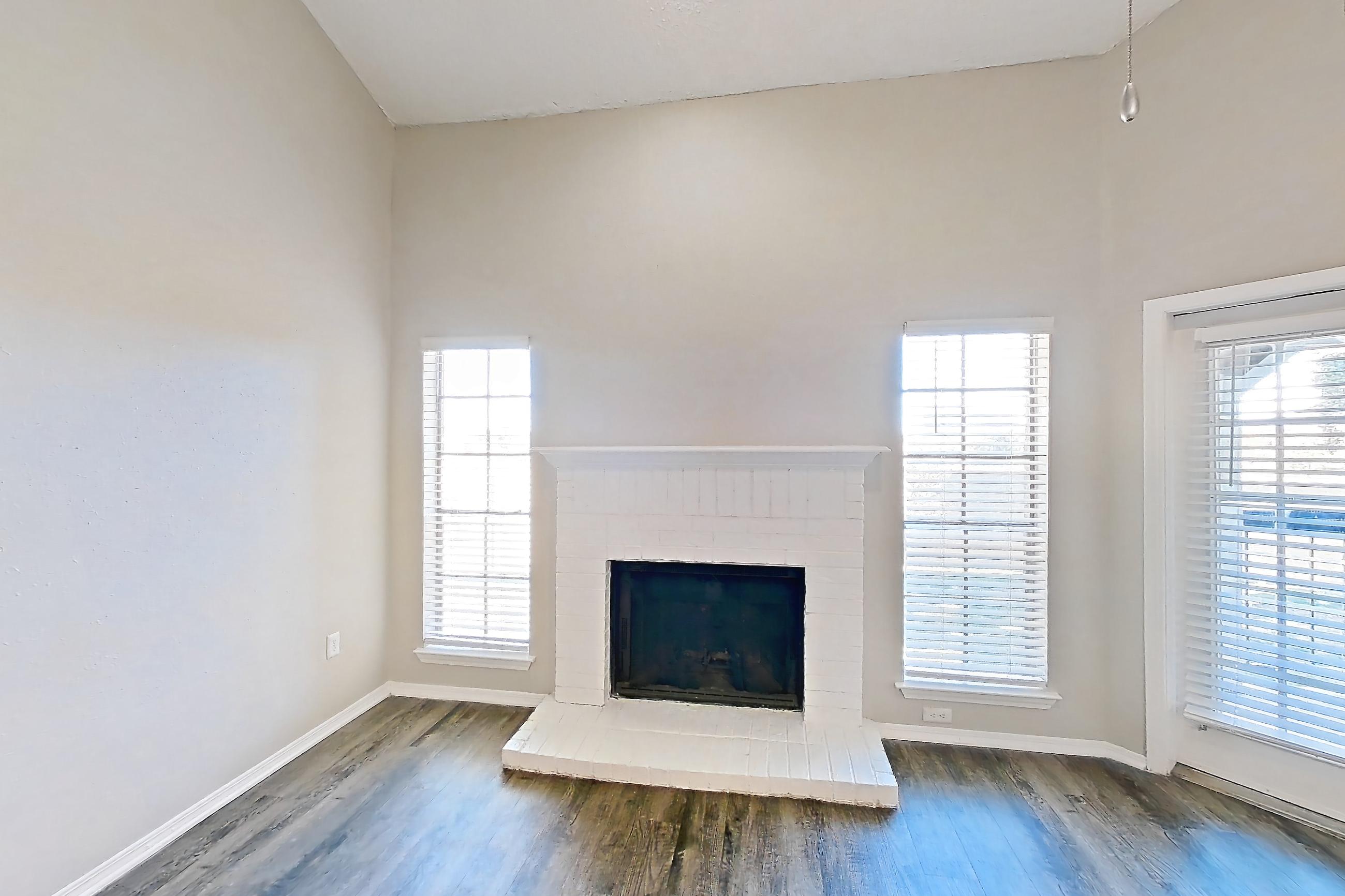 Living room with brick fireplace, dark wood-finish flooring, and fireplace, Apartment 05-0521 at The Arbors of Las Colinas