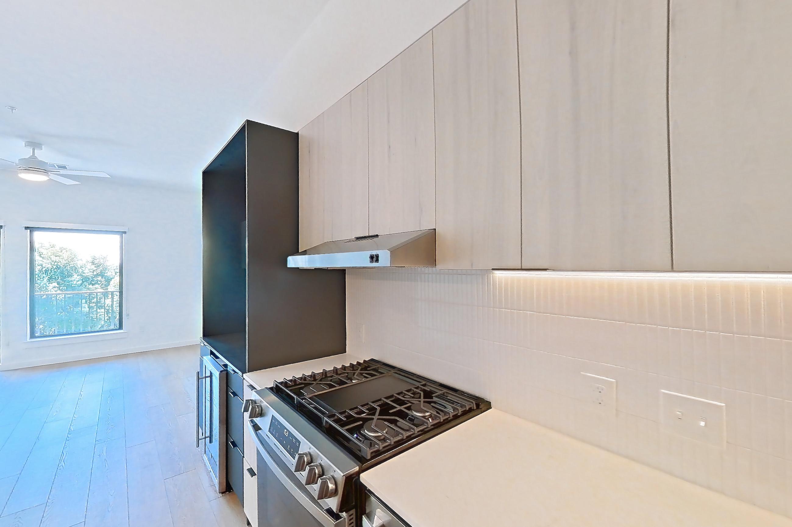 Kitchen with dishwasher, gas range, light stone countertops, light wood-finish flooring, oven/range, refrigerator, and stainless steel appliances, Apartment 0469 at Tempo at White Oak