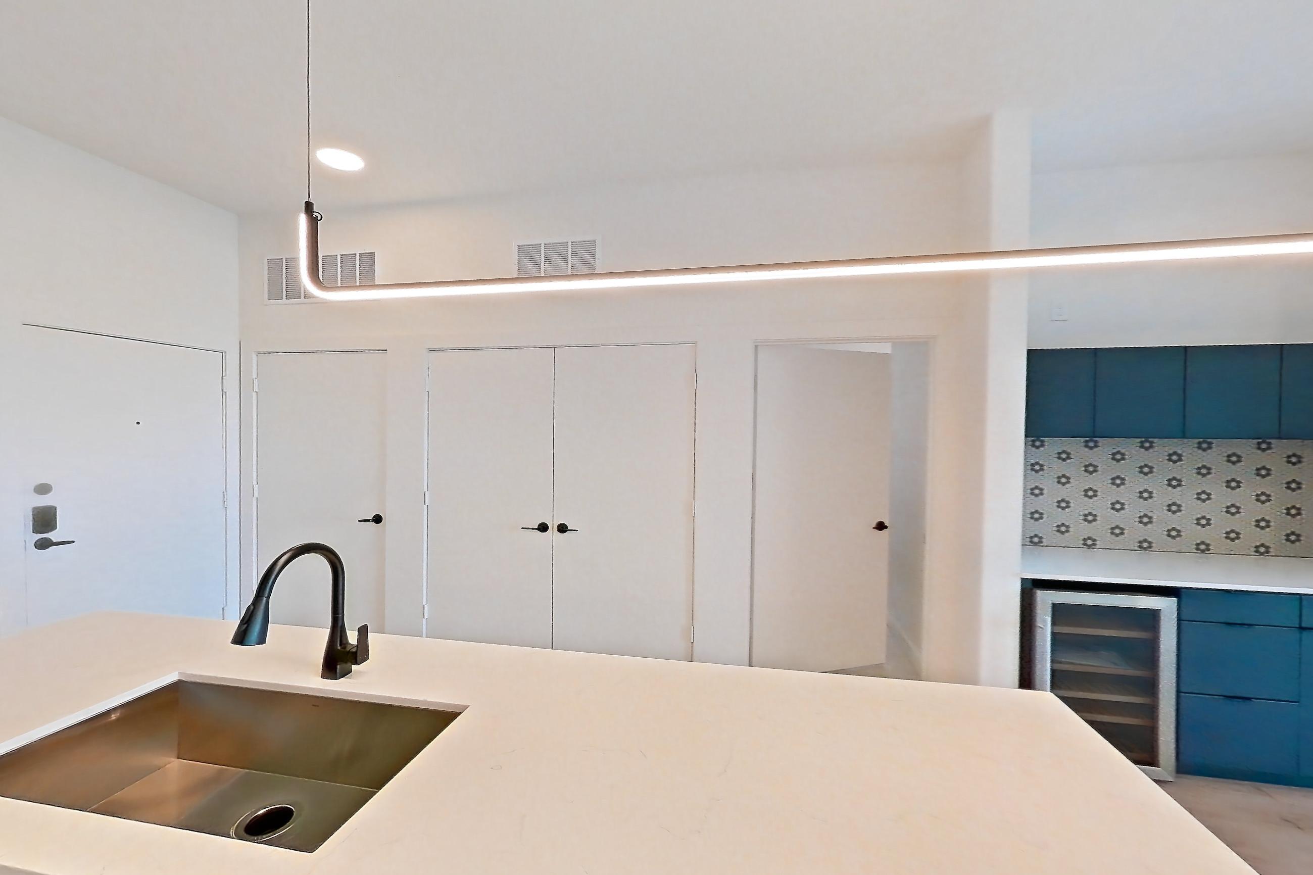 Kitchen with dishwasher, dry bar, gas range, light stone countertops, light wood-finish flooring, microwave, oven/range, range hood, refrigerator, stainless steel appliances, and wet/dry bar, Apartment 0445 at Tempo at White Oak