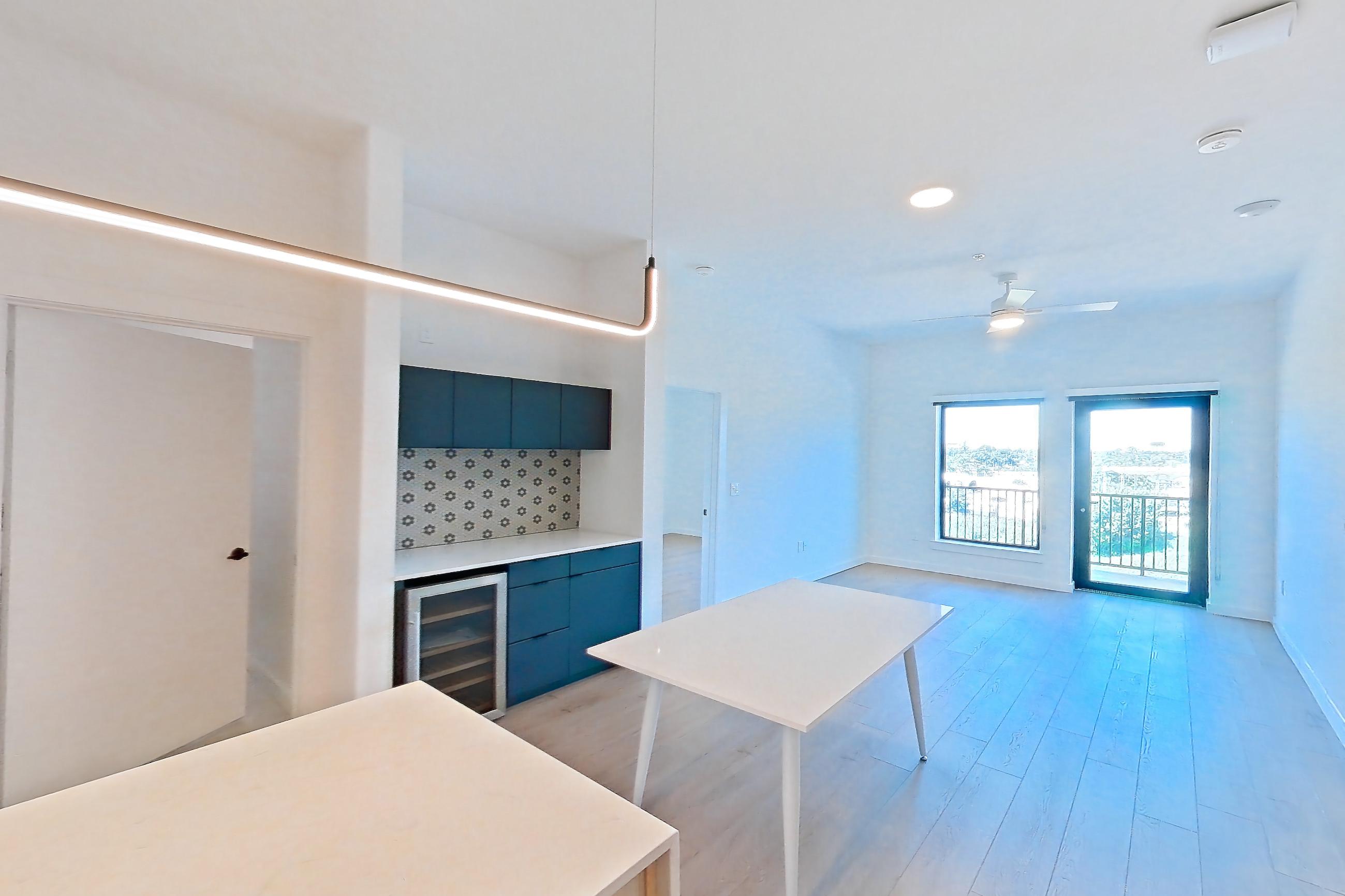 Kitchen with dishwasher, dry bar, gas range, light stone countertops, light wood-finish flooring, microwave, oven/range, range hood, refrigerator, stainless steel appliances, and wet/dry bar, Apartment 0445 at Tempo at White Oak