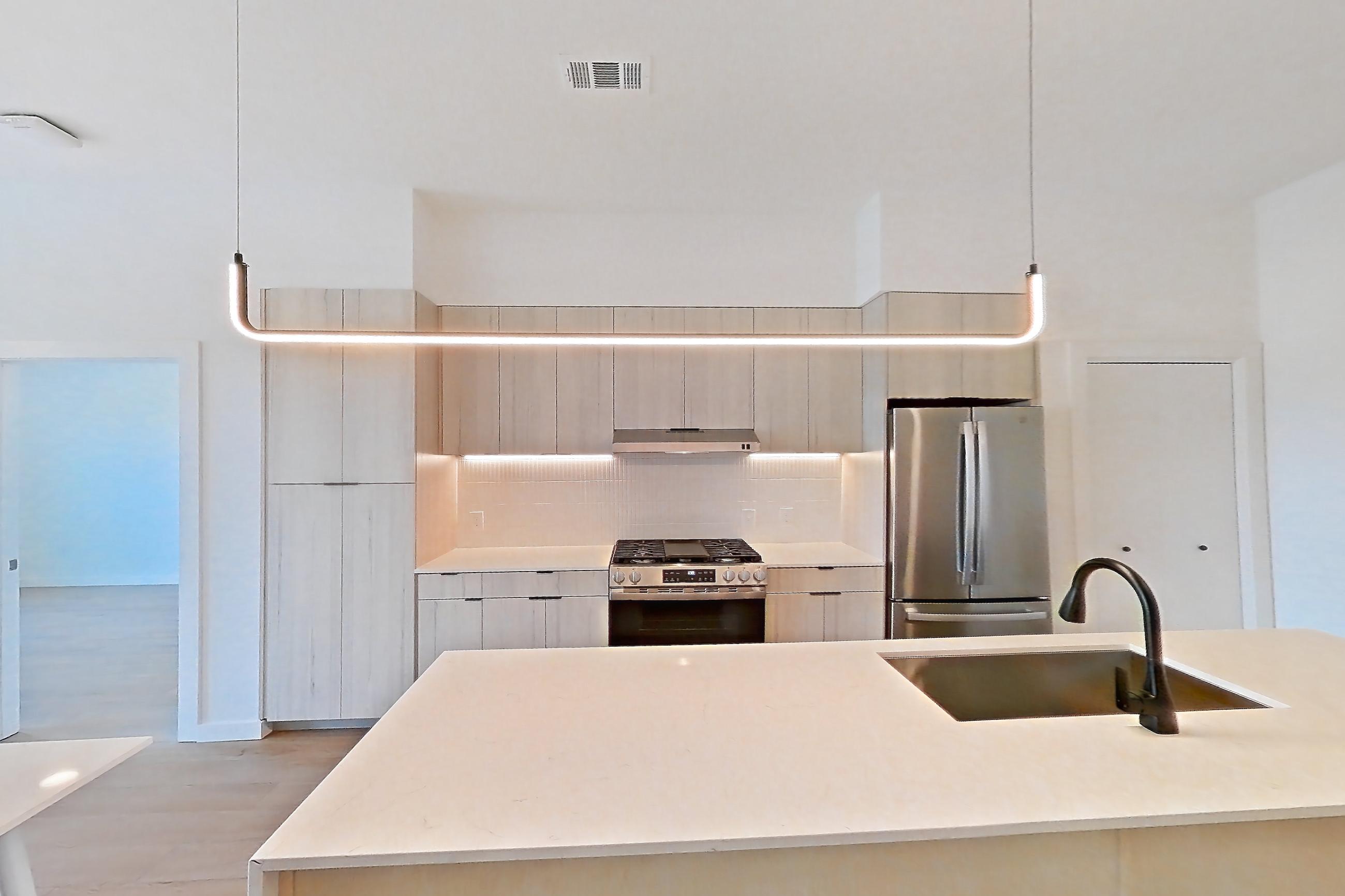 Living space with gas range, kitchen island, light stone countertops, light wood-finish flooring, oven/range, refrigerator, stainless steel appliances, and wood-finish flooring, Apartment 0445 at Tempo at White Oak
