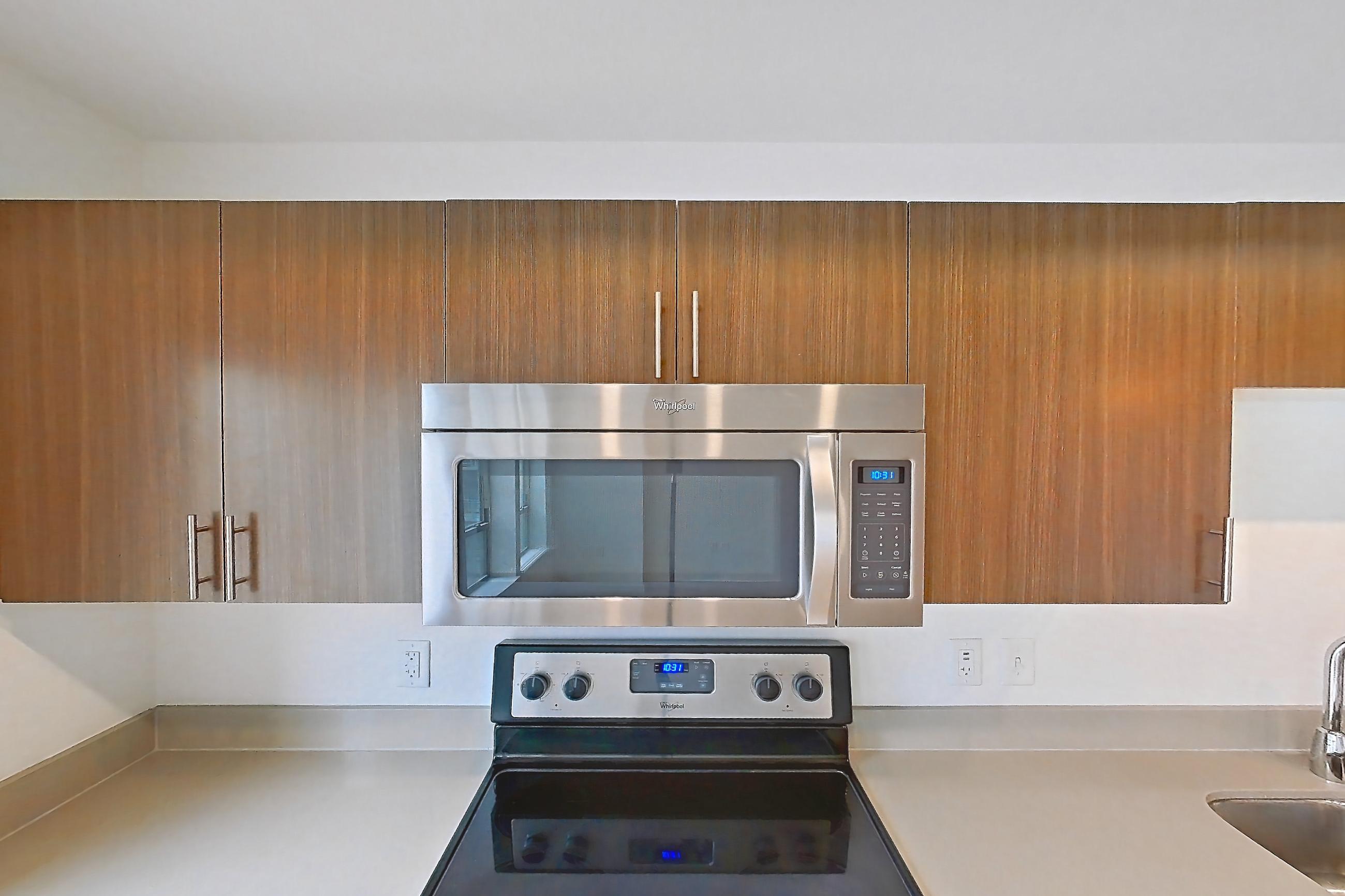 Kitchen with dishwasher, electric range, light countertops, light wood-finish flooring, microwave, oven/range, refrigerator, stainless steel appliances, and white appliances, Apartment 1013 at Cadence at Union Station